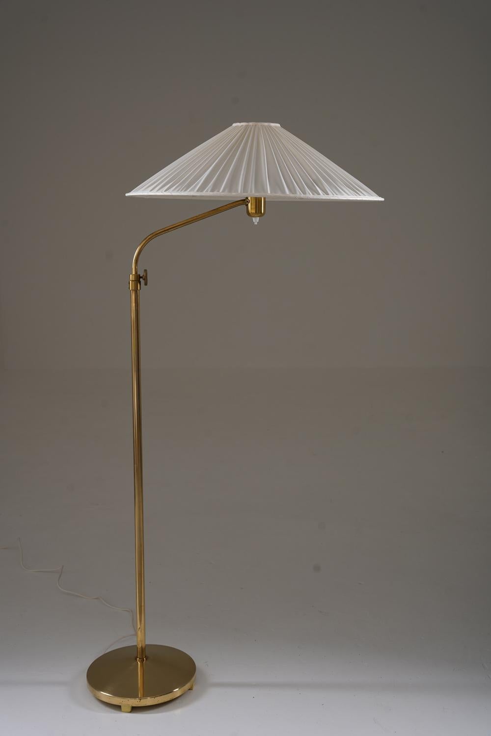 Brass floor lamp manufactured by ASEA, Sweden, in the 1940s. This elegant lamp features a slender brass stem and a wide, pleated shade made of off-white silk fabric, adding a soft diffusion to the light. The height is adjustable between 140-200 cm