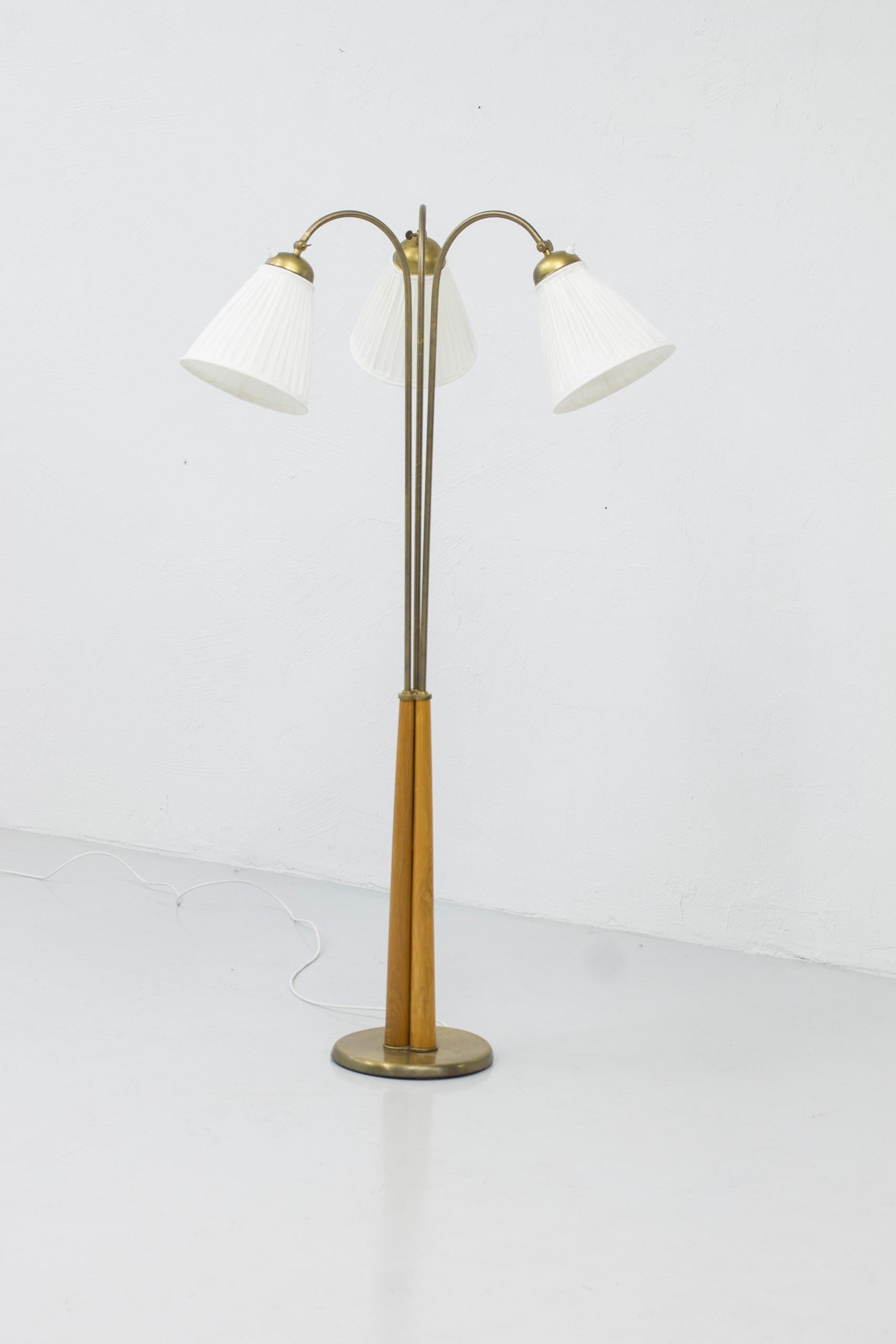 Swedish modern floor lamp designed and produced in Sweden around the 1940s. Made from brass with solid elm lamp stem. Three adjustable arms both in angle of the hade as well as position. Light switches on all lamp shades in working order. Very good