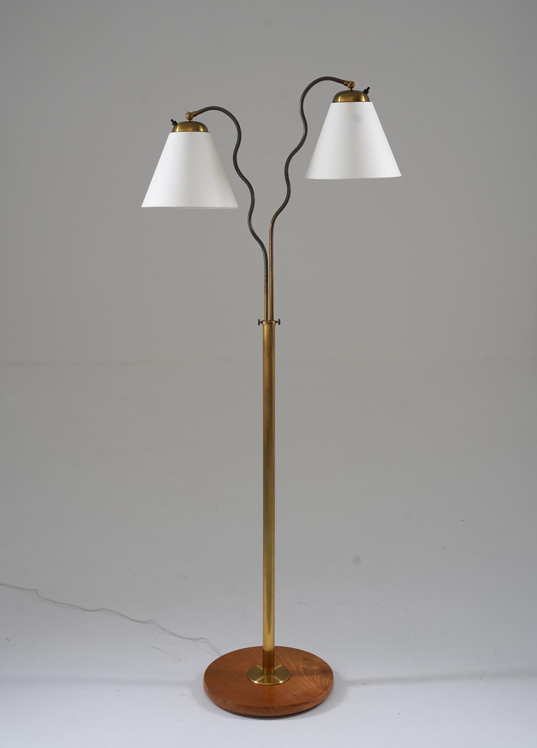Lovely Swedish Modern floor lamp manufactured in Sweden, 1940s. 
The lamp consists of a wooden base with a brass rod, supporting two wave-shaped swivel arms that hold the shade. 
The height is adjustable between 139-164cm (55-65