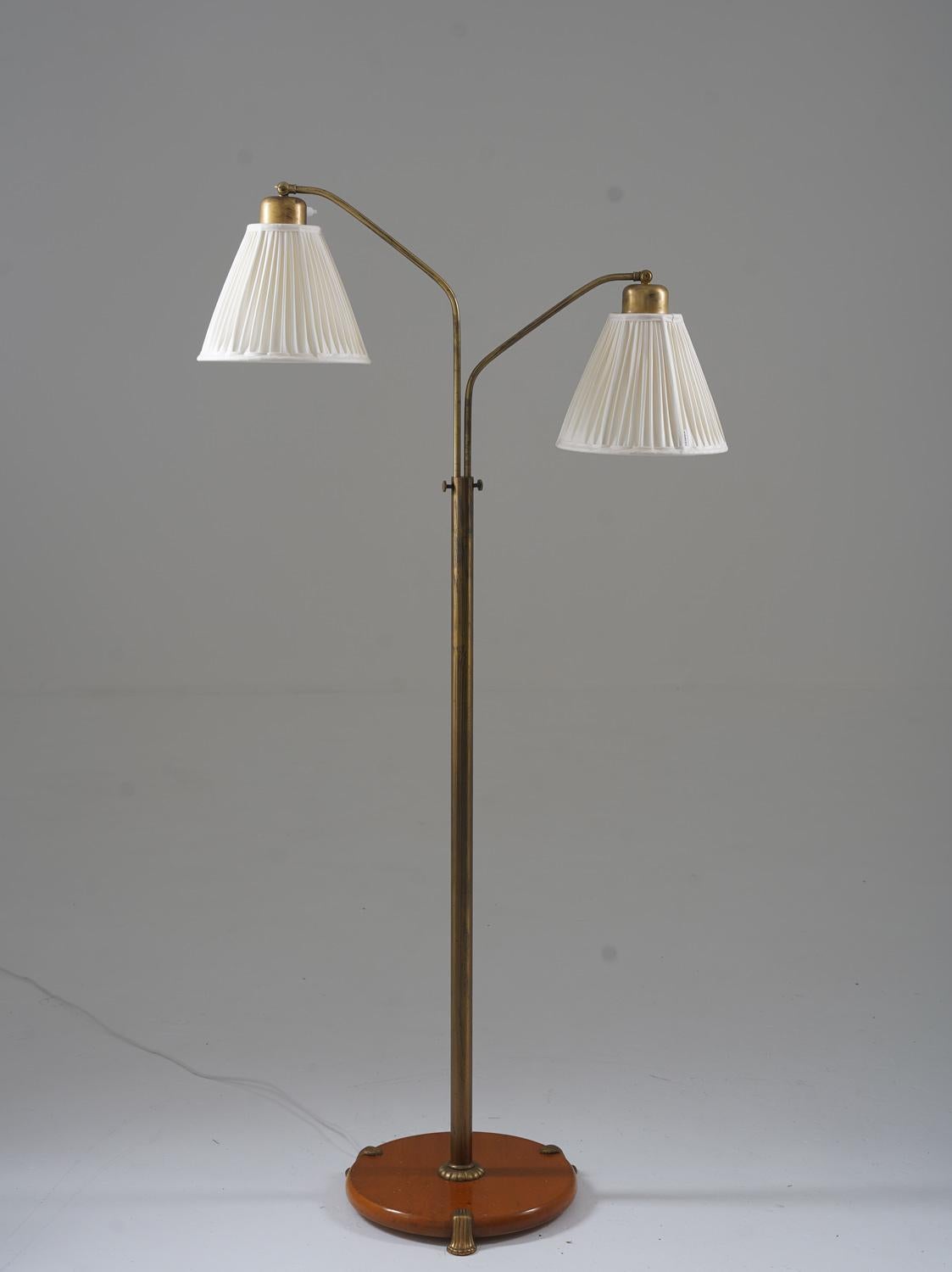 Lovely Swedish Modern floor lamp manufactured in Sweden, 1940s. 
The lamp consists of a wooden base with a brass rod, supporting two swivel arms that hold the shades. 
The height is adjustable between 125-150cm (49-59