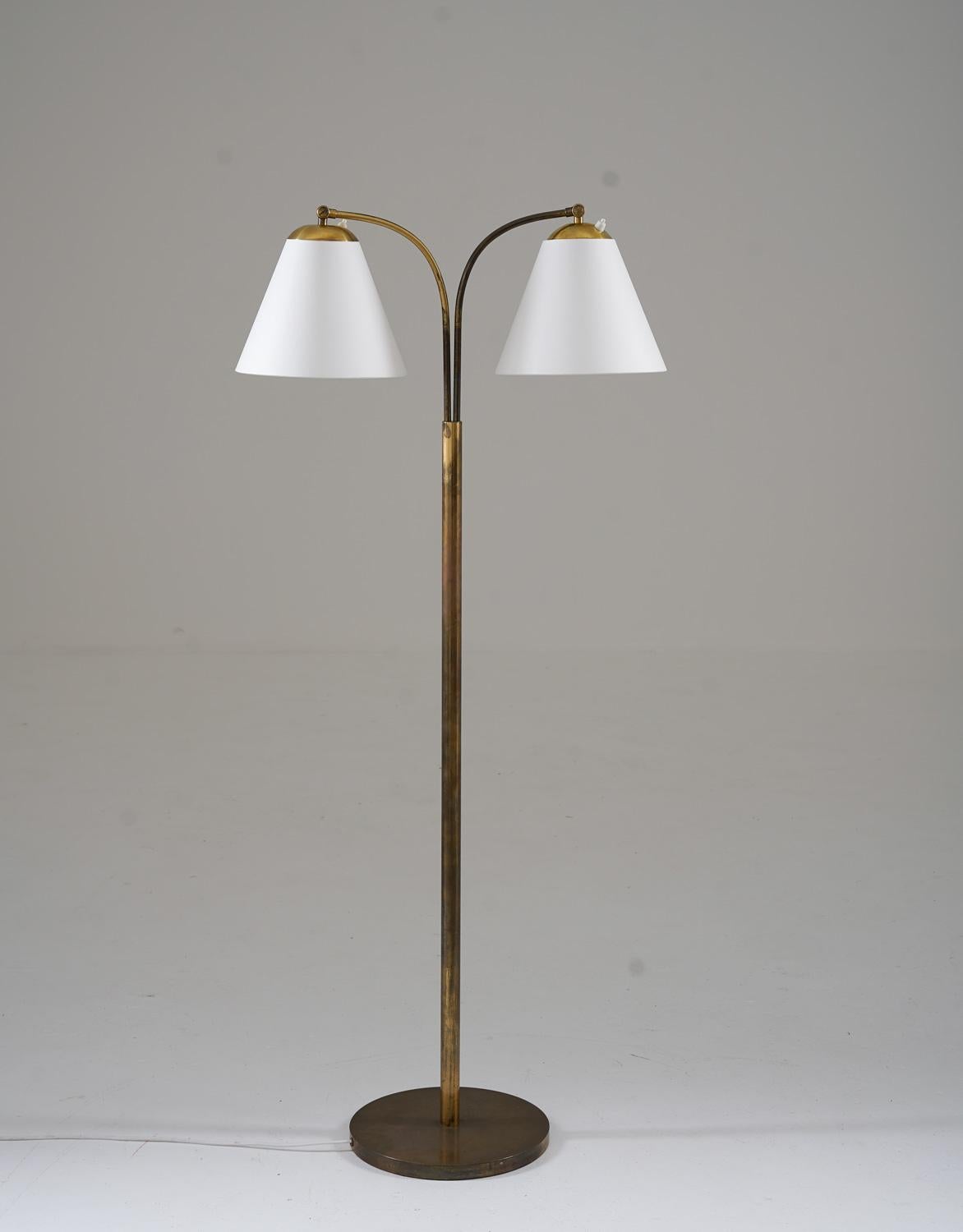 This is a lovely Swedish Modern floor lamp that was manufactured in Sweden during the 1940s. The lamp features a brass base and rod, which supports two swivel arms that hold the shades. The swivel arms are adjustable in height, making it easy to