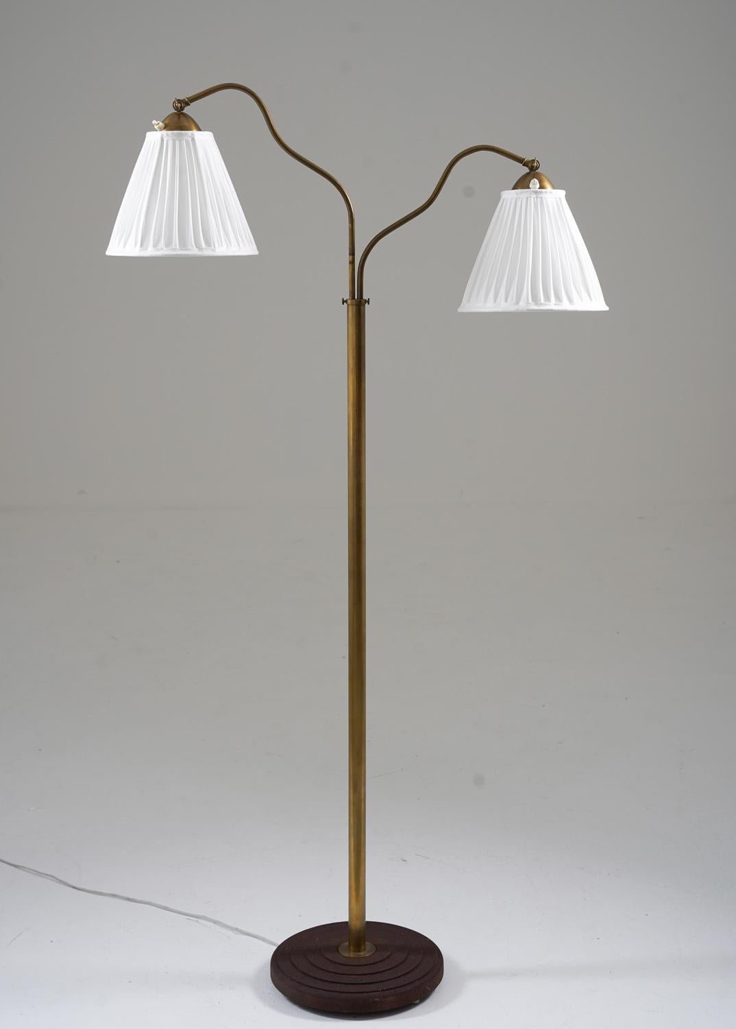 This is a lovely Swedish Modern floor lamp that was manufactured in Sweden during the 1940s. The lamp features a solid iron base and a brass rod, which supports two swivel arms that hold the shades. The swivel arms are adjustable in height, making