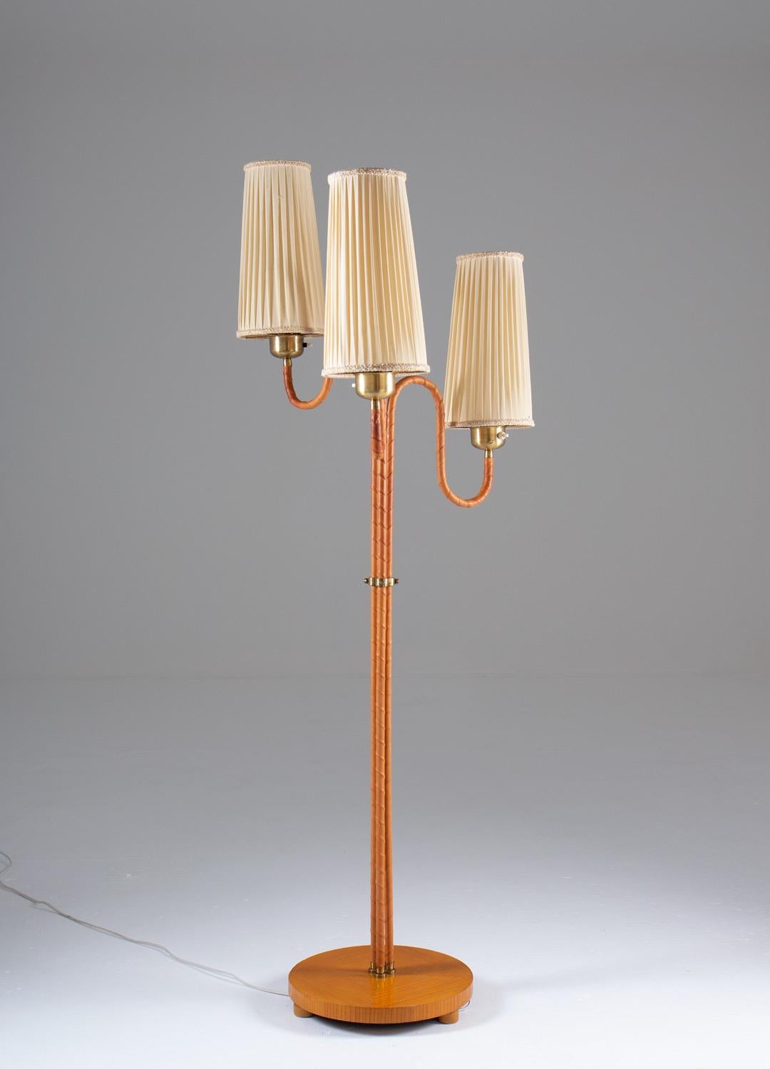 Rare floor lamp manufactured in Sweden, 1930-40s. 
This floor lamp consists of three leather webbed bases, connected by a brass divider and a wooden foot. Each base holds a light source, hidden by off-white fabric shades.

Condition: Good vintage