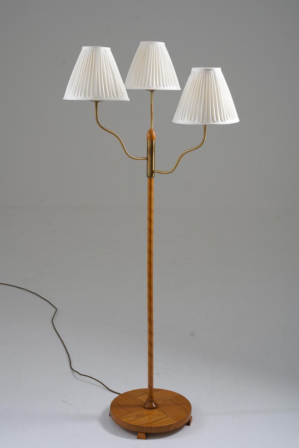 Rare floor lamp manufactured in Sweden, 1930-1940s. 
This floor lamp consists of a wooden base and a rod webbed in elm-veneer. Three brass rods holds the light sources, hidden by fabric shades.

Condition: Good vintage condition with new