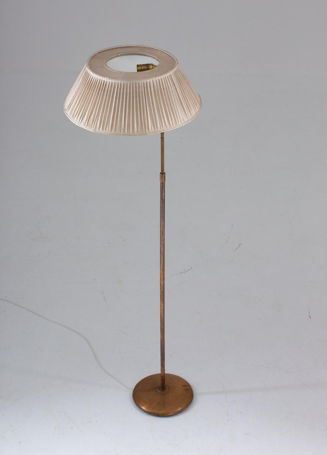 Scandinavian midcentury floor lamp in brass, attributed to Nordiska Kompaniet (NK), 1930s.
This rare floor lamp is made of solid brass, with original fabric shade supported by a white uplight metal shade. It offers two light sources, one uplight