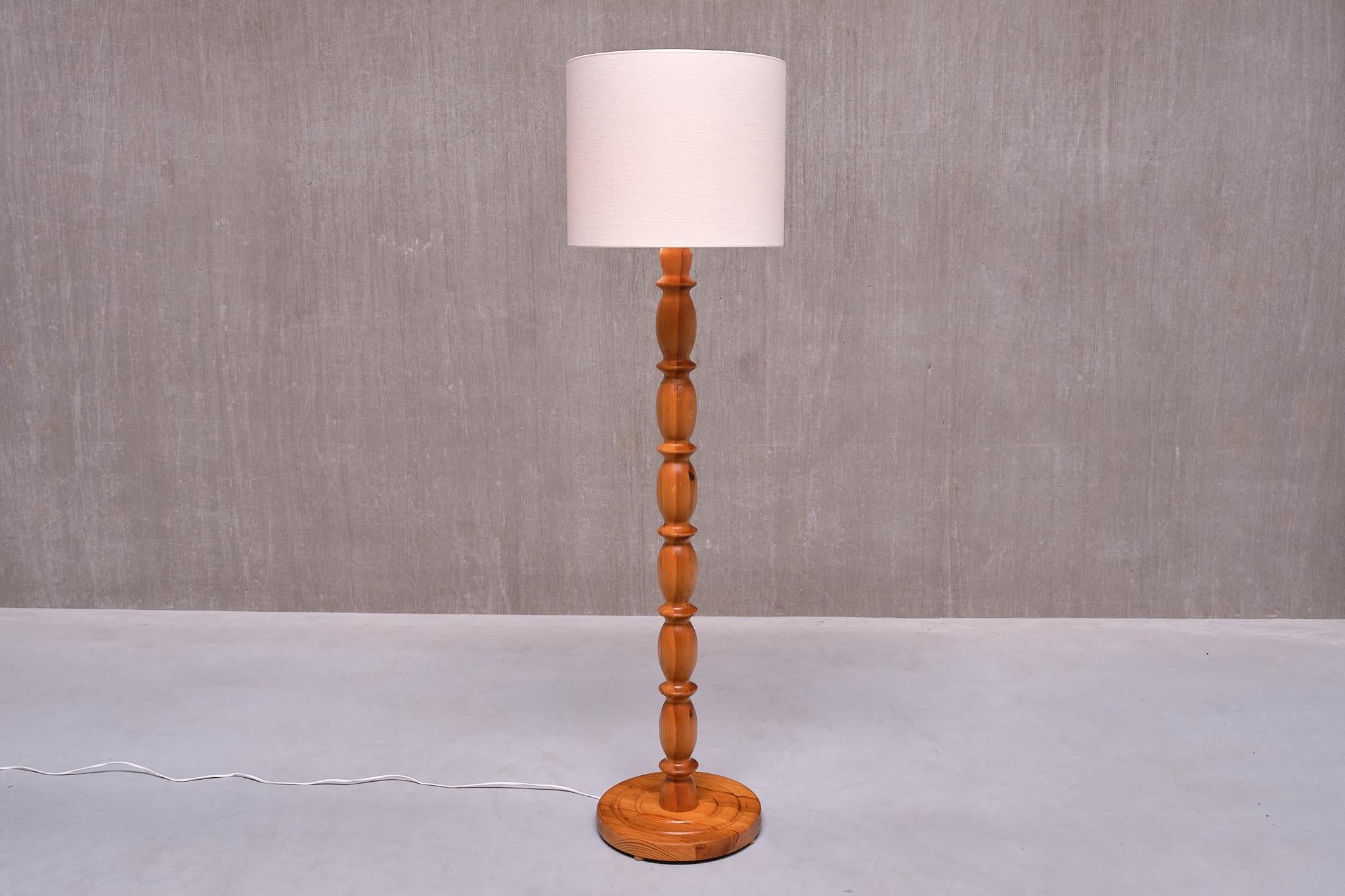 This striking tall floor lamp was produced in Sweden in the 1960s.

The Swedish Modern design is characterized by a central stem crafted from solid pine wood, featuring alternating elliptical and disc-shaped carved elements. The circular base,