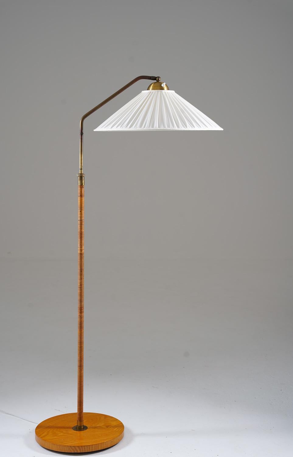 Lovely Swedish modern floor lamp manufactured in Sweden, 1940s. 

The lamp consists of a wooden base, supporting a brass rod with rattan webbing. The shade is fixtured on a swivel arm, which is adjustable in height (130-160cm, 51-63