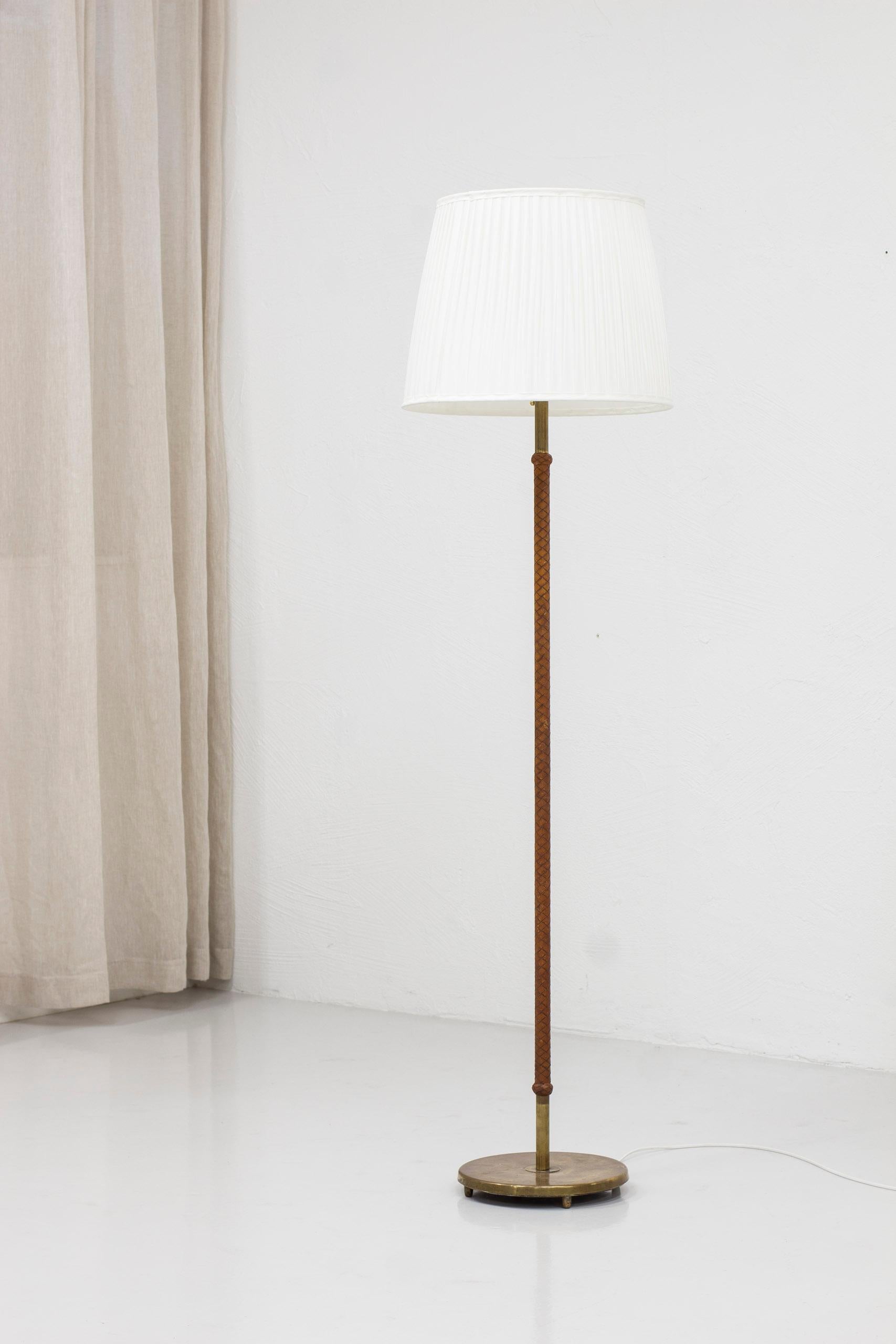 Floor lamp designed and produced in Sweden during the 1940-50s. Made from brass with original braided leather wrapping on the stem. The original lamp shade has been re-sewn with off white chintz fabric to replicate the original. Light switch on the