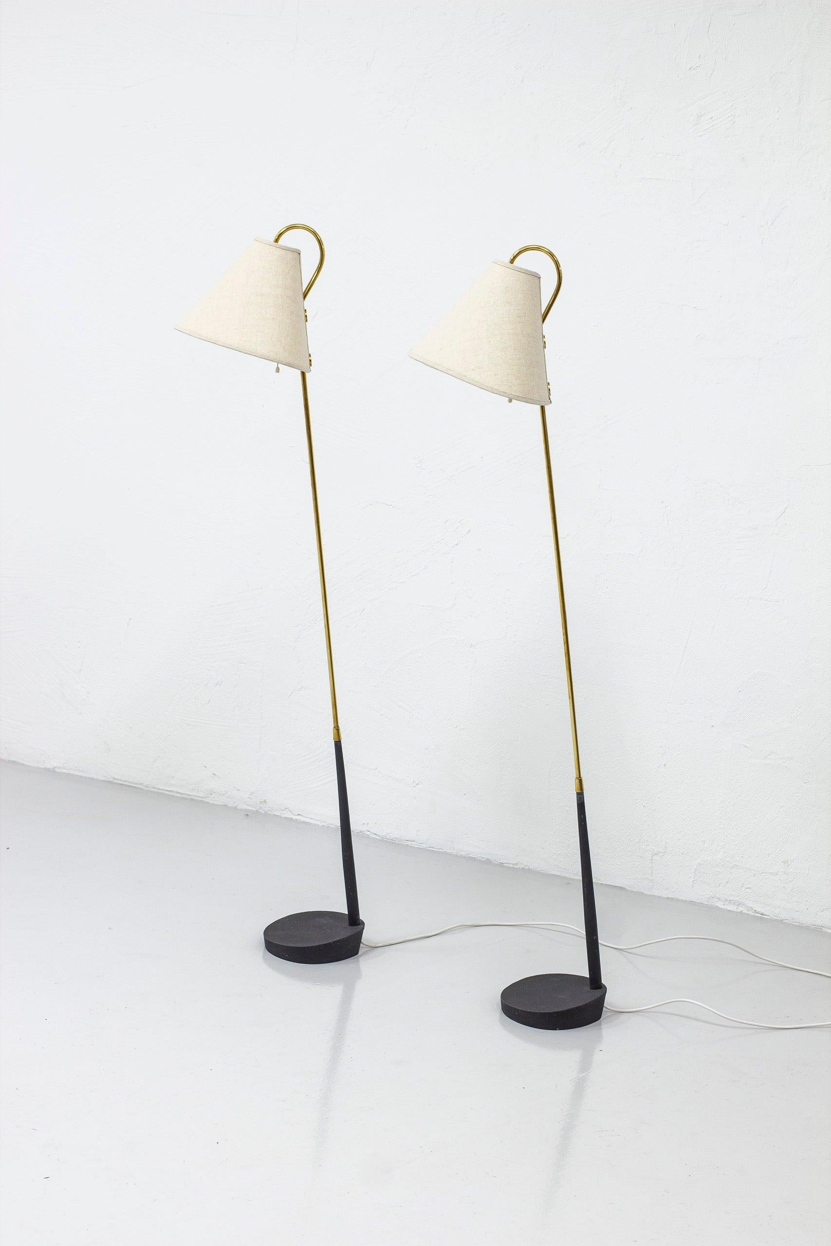 Ein Paar Stehlampen, hergestellt in Schweden von ASEA Belysning. Hergestellt in den 1950er Jahren. Sockel aus Gusseisen mit grauer Farbe und poliertem Messing. Neue Lampenschirme aus natürlichem Leinenstoff. Zugschnur-Lichtschalter an beiden Lampen