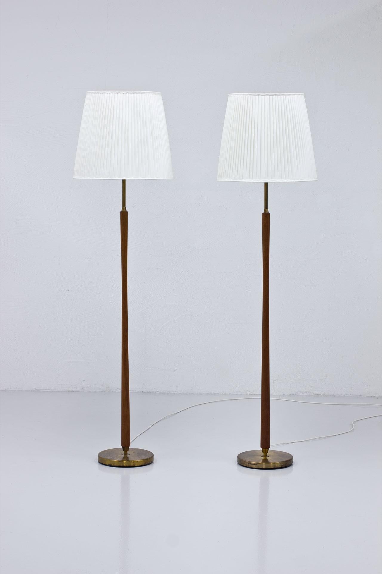 Pair of floor lamps manufactured by ASEA in Sweden during the 1940s-50s.
Made from brass with teak stem and new hand sewn shades in off-white chintz fabric. 
Four light bulbs on each lamp with two light switch. One uplight source, the others