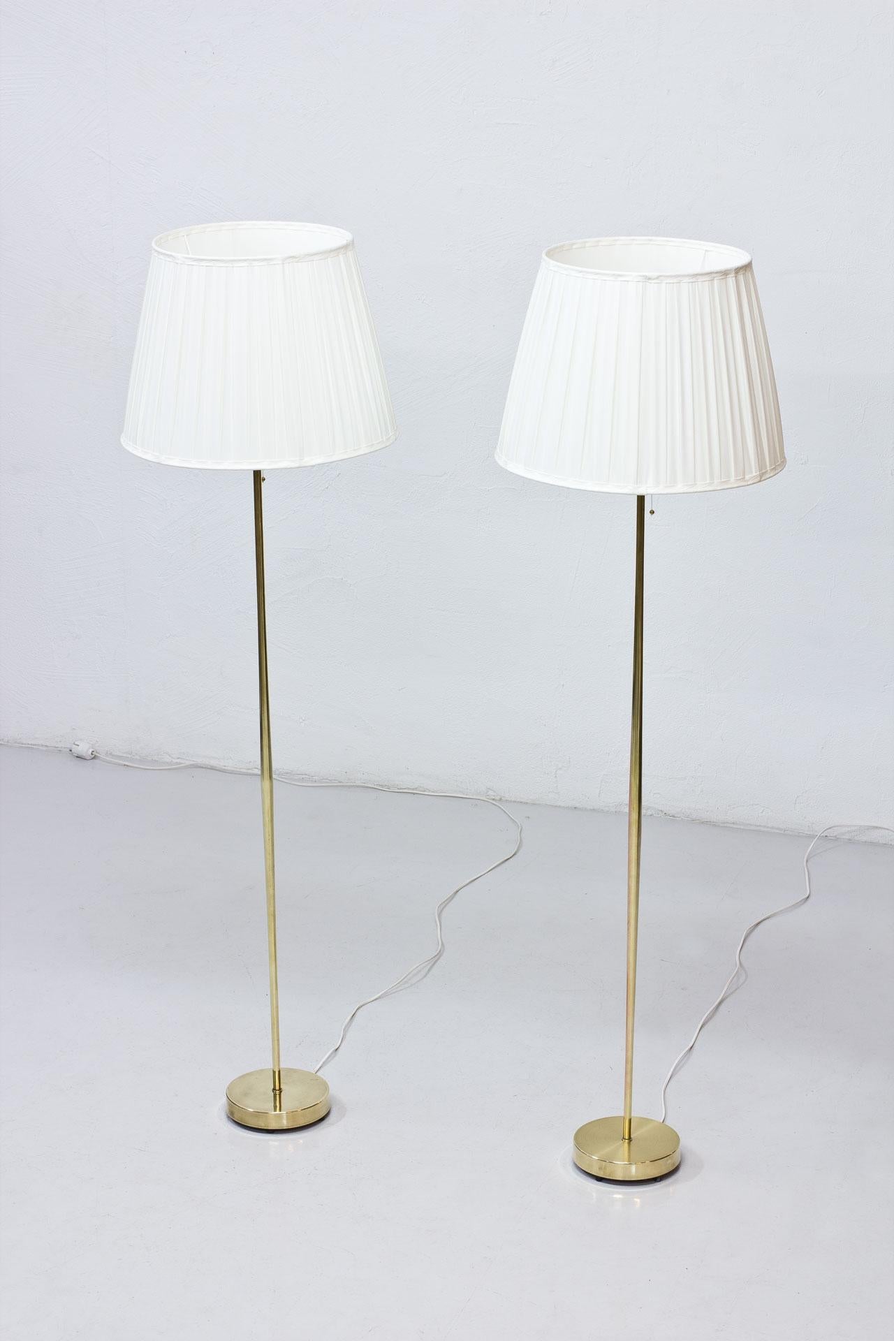 Pair of floor lamps manufactured by Falkenbergs Belysning in Sweden during the 1950s. 
Polished brass stem. 
Lamp shades reupholstered in a box pleated off-white chintz fabric. 
Rewired. Light switch on the brass fittings. Signed on the bottom.