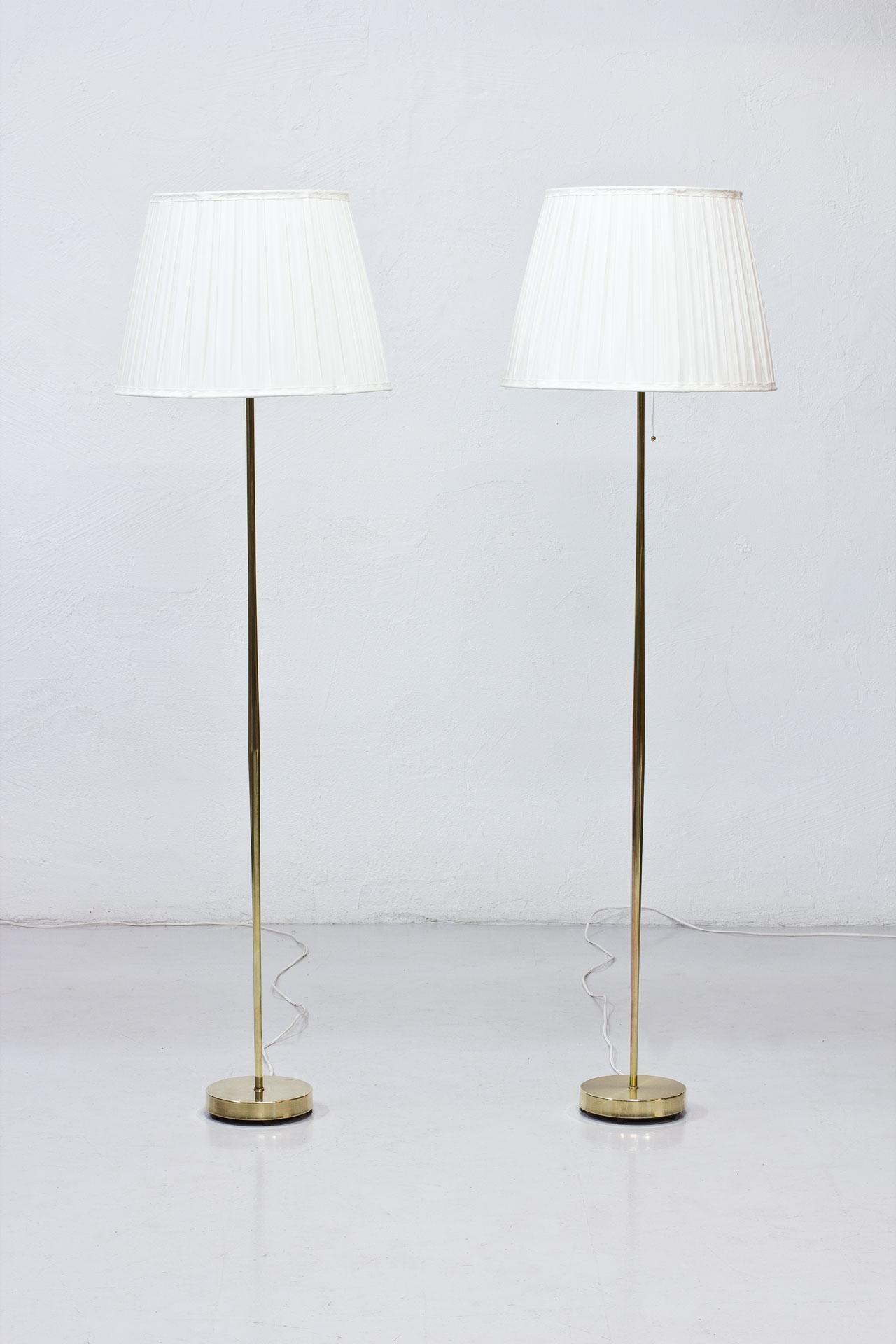 Pair of floor lamps manufactured by Falkenbergs Belysning in Sweden during the 1950s. Polished brass stem. Lamp shades reupholstered in box pleated off-white chintz fabric. Rewired. Light switch on the brass fittings. Signed on the bottom.