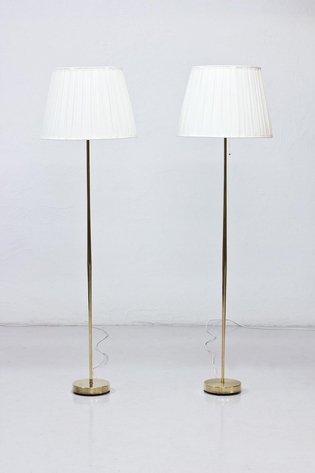 Beautiful and elegant pair of floor lamps manufactured in Sweden during the 1950s by Falkenbergs Belysning. Made from polished brass stem and fittings with new box pleated lamp shades in off- white chintz fabric. New electricity with light switch on