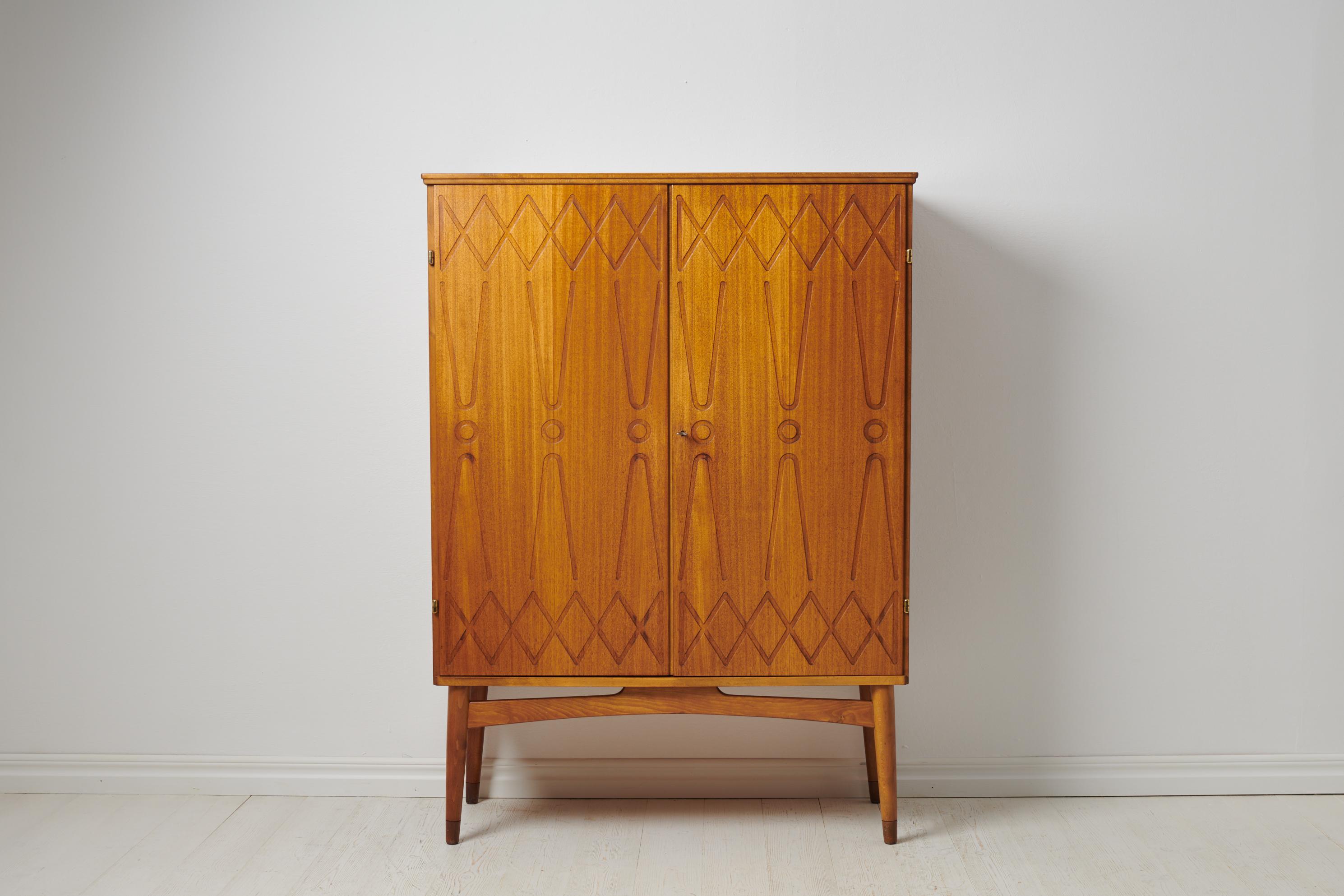 Swedish modern teak cabinet ”Rickard” designed by Kirke Nielsen and made by Abrahamssons Möbelfabrik in Smålands Taberg. The cabinet is from the mid 20th century, during the 1950s and features a pair of doors with embossed decor. The doors open to