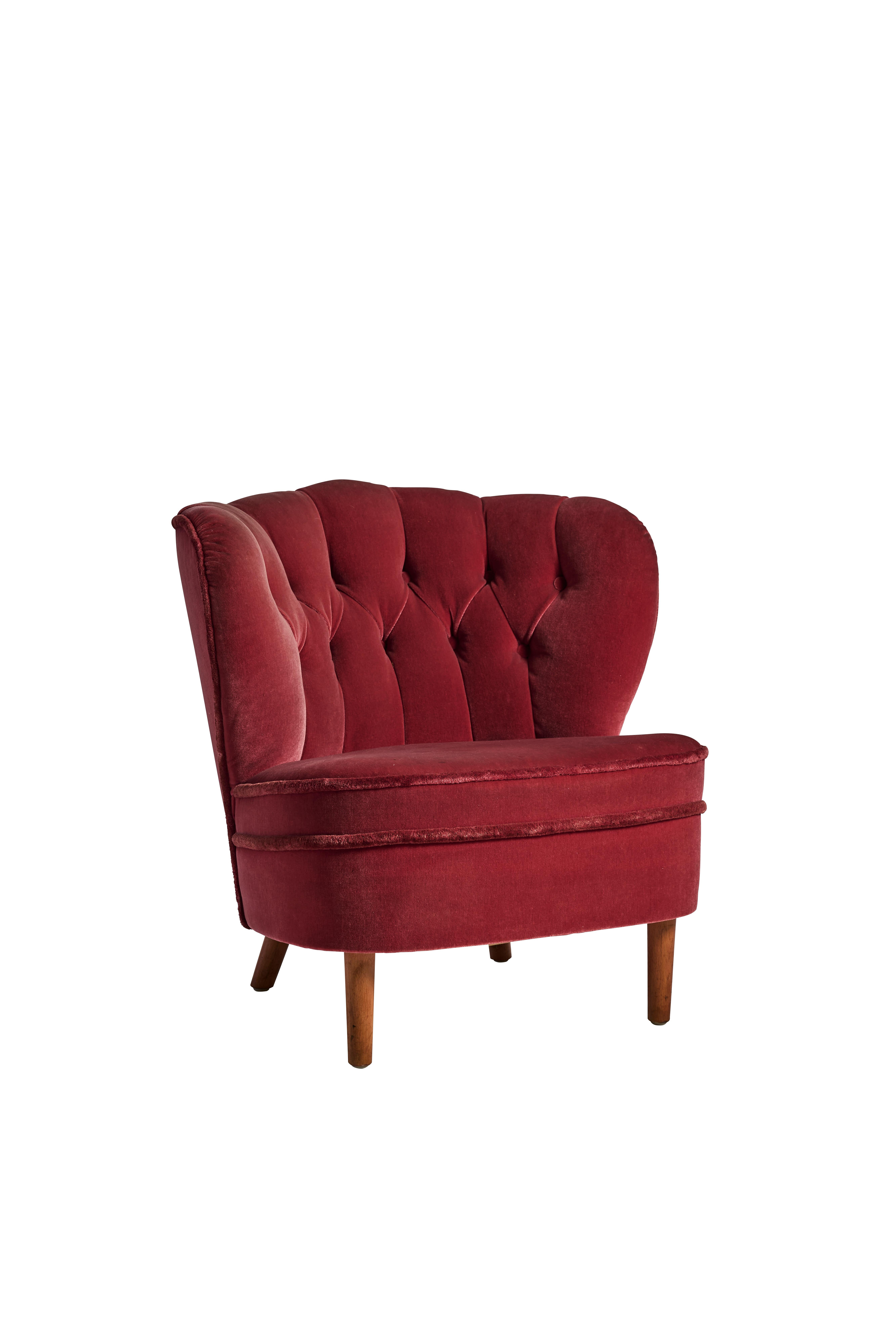 Dieser elegante und zeitlose Sessel der schwedischen Moderne aus den 1940er Jahren zeichnet sich durch seinen originalen rubinroten Samtbezug und eine skulpturale, feminine Silhouette aus. Die tiefe, mit Knöpfen getuftete Rückenlehne, die sanft
