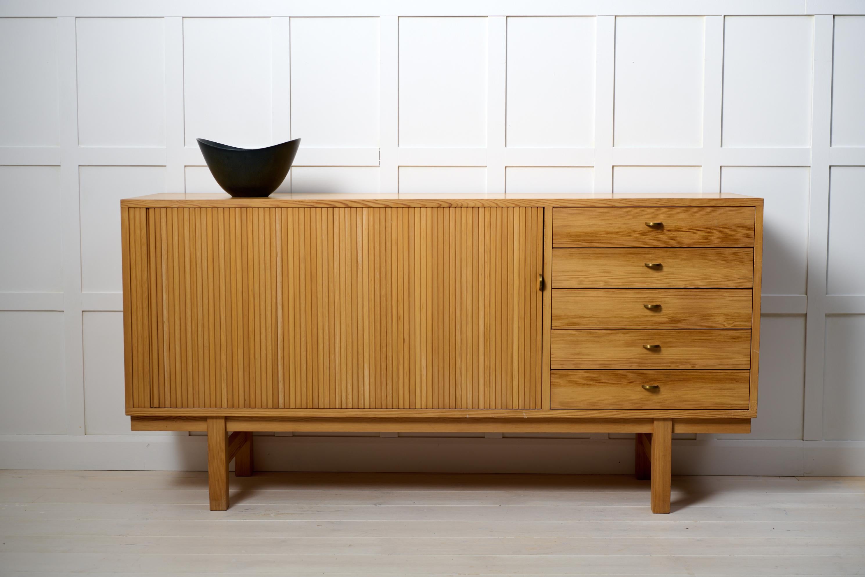 Swedish modern low sideboard from around 1960 to 1970. The sideboard is made in pine which is unusual to see. It has five drawers and a jalousie-door. Good vintage condition. The sideboard has some minor traces of use. The brass drawer pulls to the