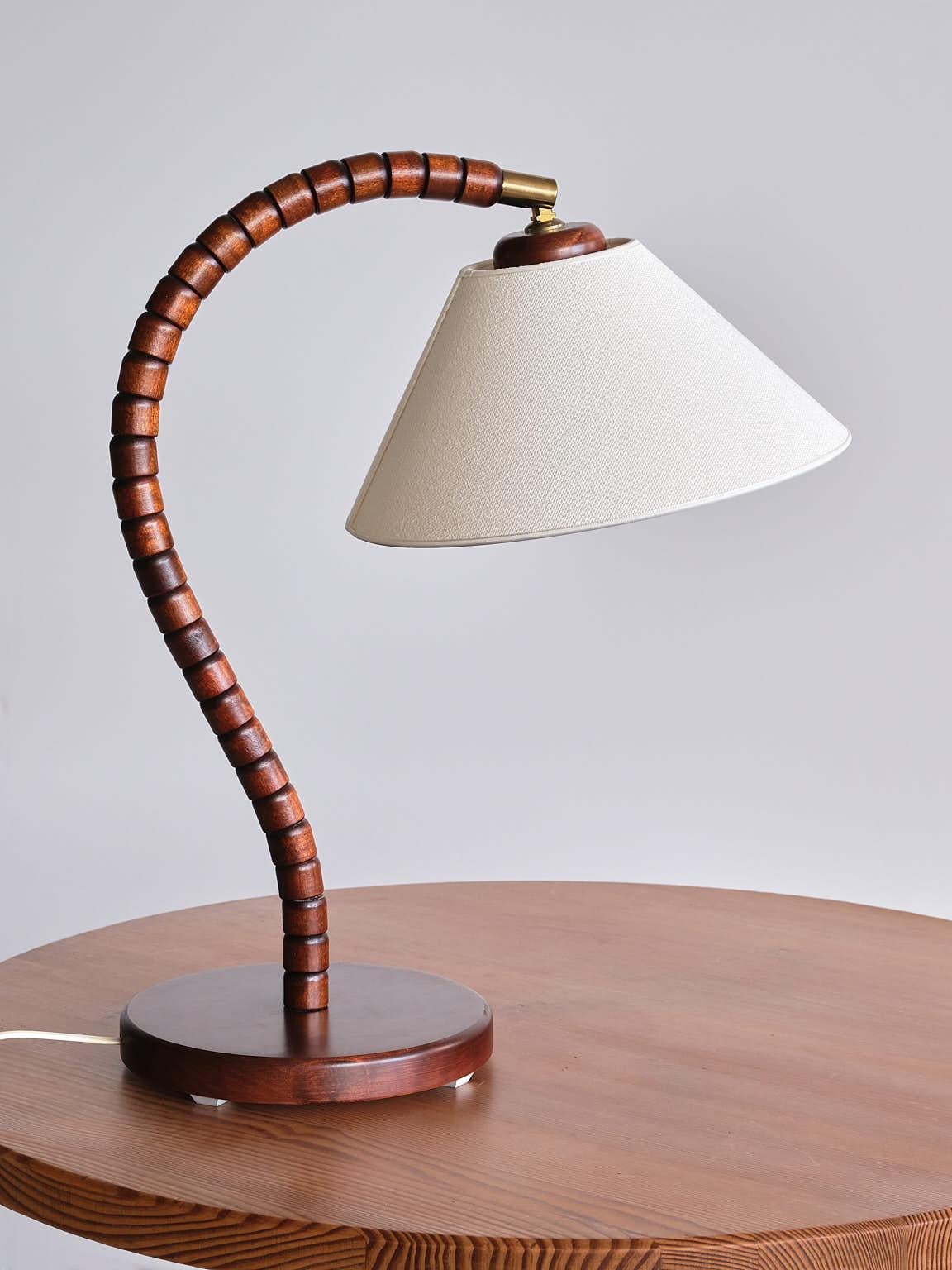 This striking table lamp was produced by Markslöjd in Kinna, Sweden in the 1970s. The design is marked by the sculptural, organic shaped frame resting on a circular base. The base is made of solid stained beech wood. Brass and beech wood fitting.