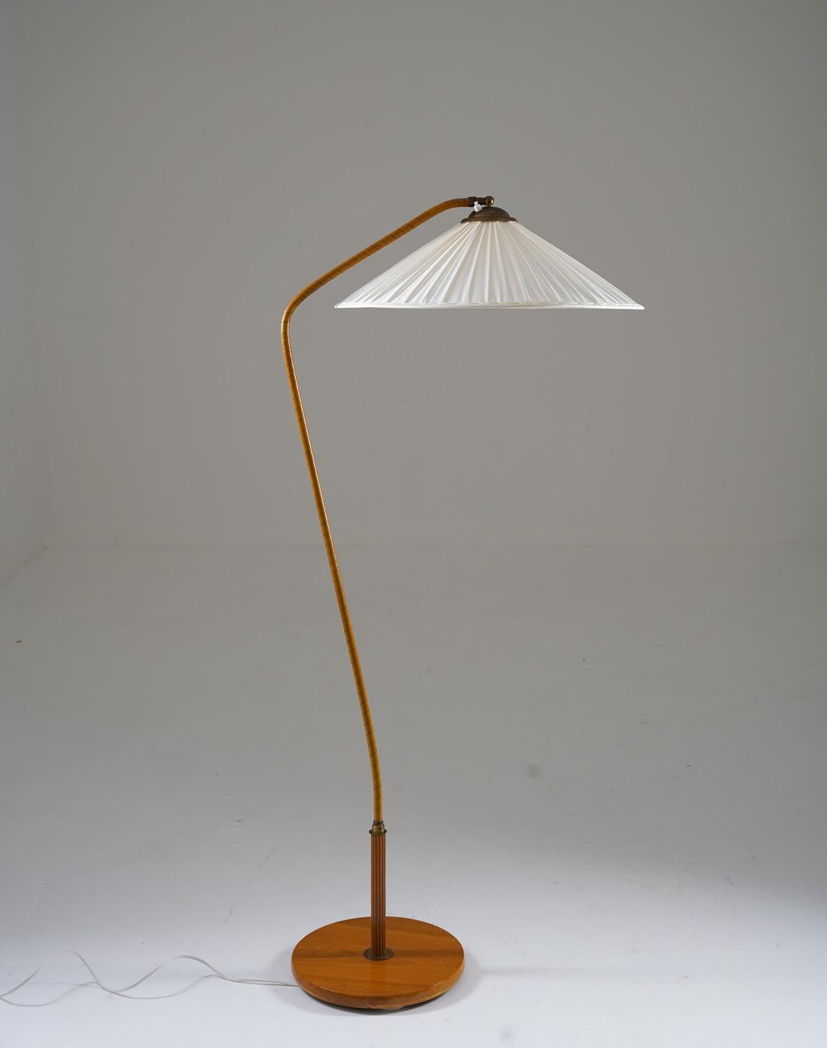 Beautiful floor lamp, manufactured in Sweden ca 1940.

This floorlamp consists of a beautifully curved pole, webbed in original cognac-colored faux leather. The pole is supported by a large wooden foot with brass details. The impressive fabric