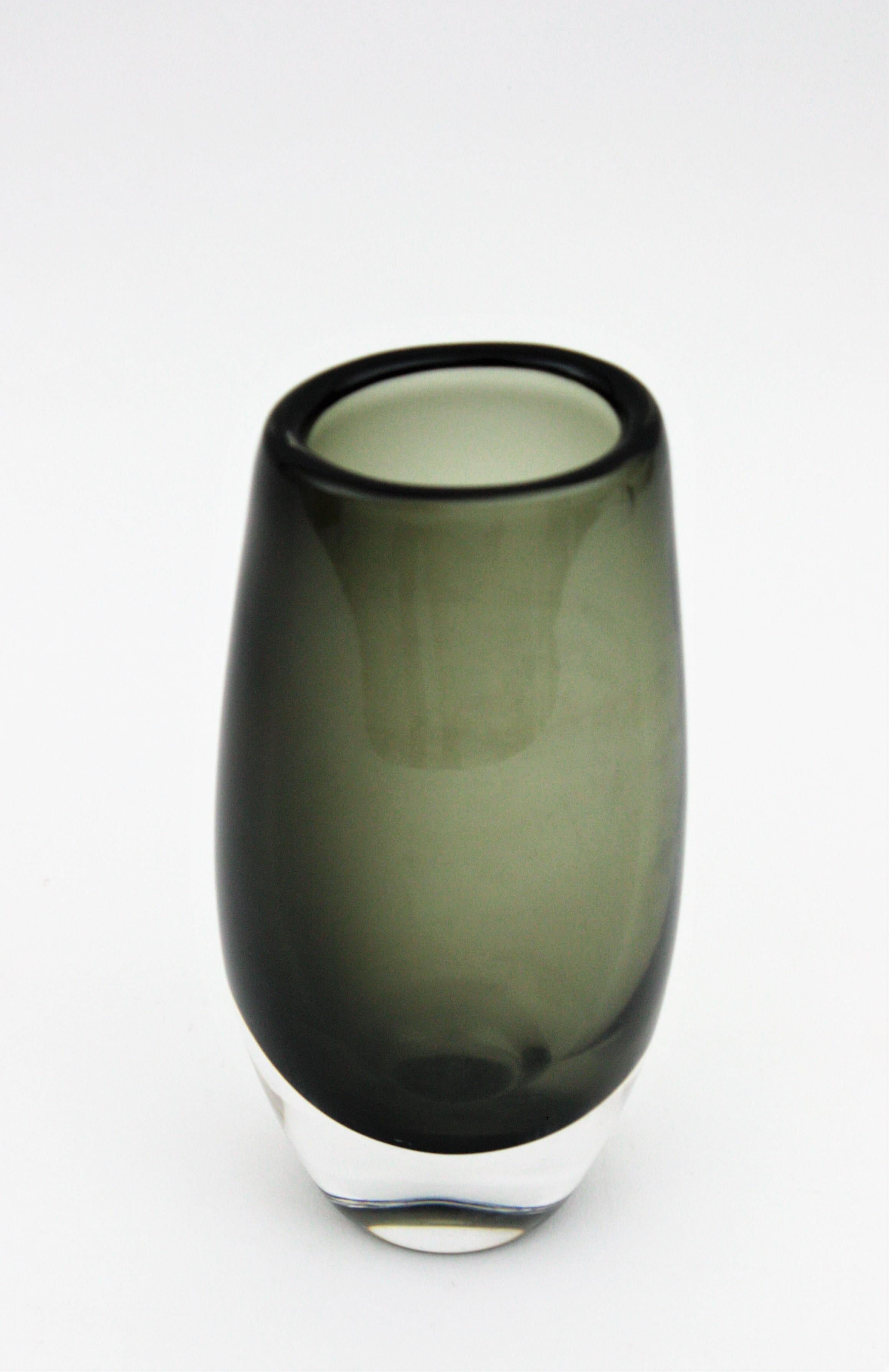 Elegante Vase aus rauchgrauem und klarem Sommerso-Glas. Entworfen von Nils Landberg und hergestellt von Orrefors. Schweden, 1970er Jahre.
Diese mundgeblasene Glasvase hat ein wunderschönes Design mit rauchgrauem Glas, das in Klarglas eingefasst