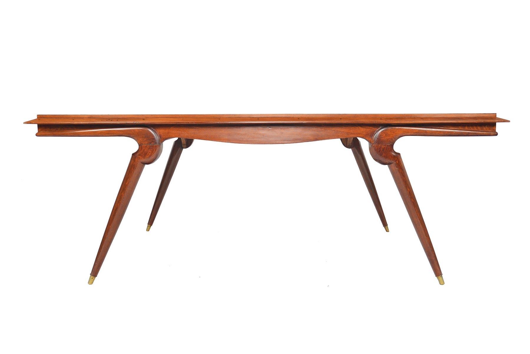 This outstanding Swedish modern “library” table was crafted from stained oak in the 1940s. The large table surface sits a few inches higher than the standard dining table. Table features dramatic saber- shaped legs caped in brass. In excellent