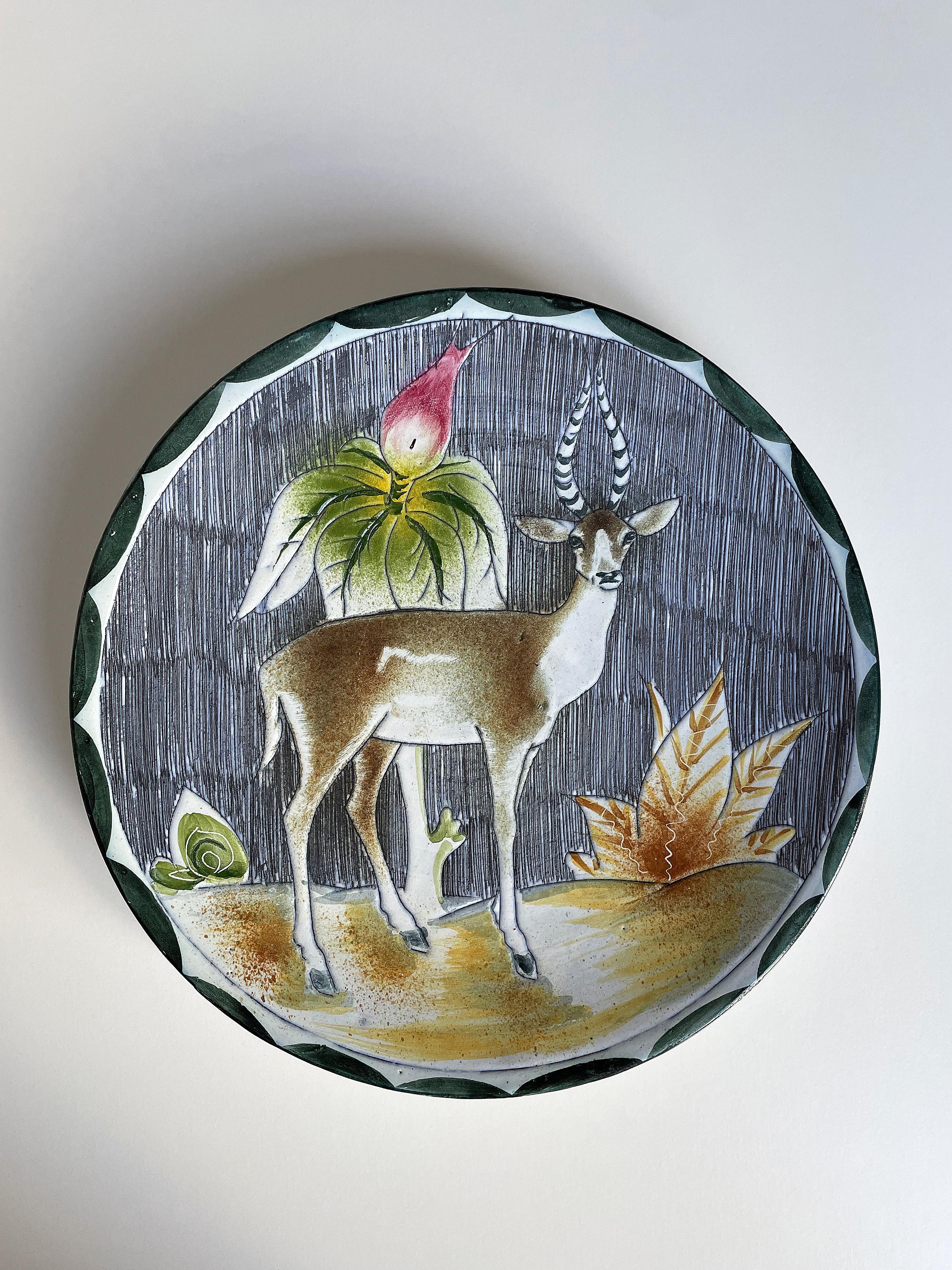 Vintage handmade fully glazed Swedich midcentury modern wall platter / centrepiece with organic, floral decor depicting a gazelle with a direct gaze surrounded by vegetation in brown, ochre, green, white and bright pink colors on a striped dark blue