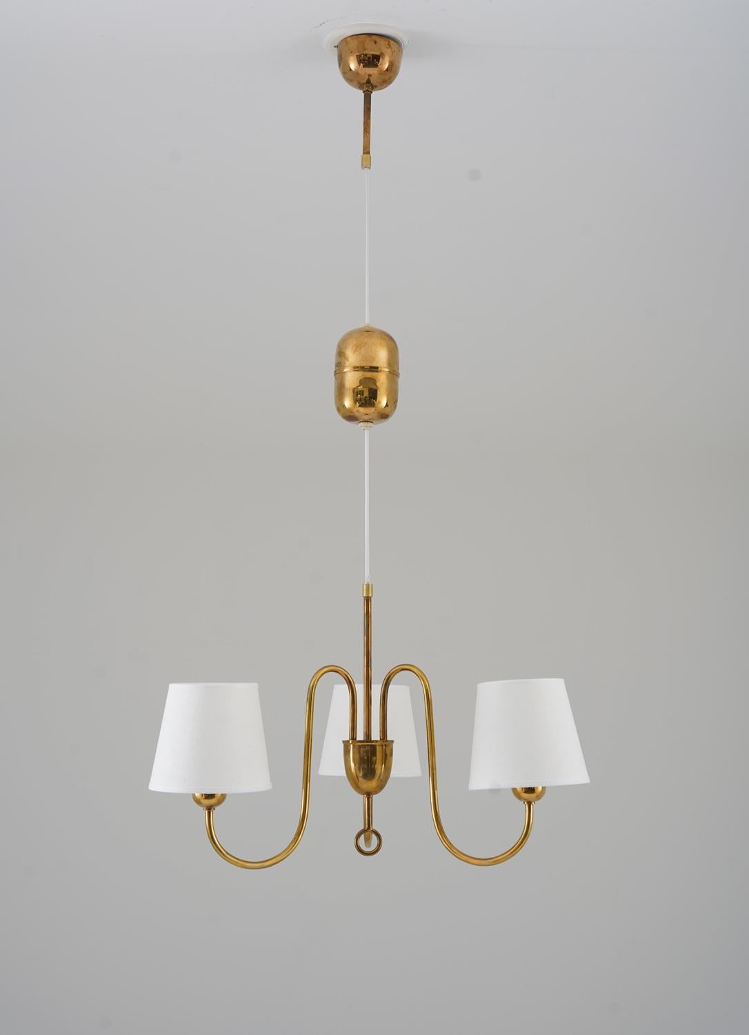 Beautiful pendant in brass with adjustable height, manufactured in Sweden, 1940s.
This pendant features three light sources, hidden by fabric shades (new). The shades are connected to a center piece, where the brass rod, holding the lamp, is