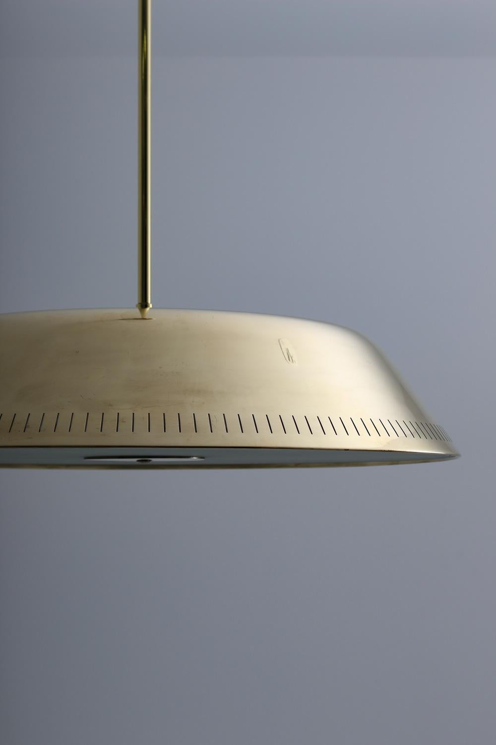 Pendant in frosted glass and brass by Harald Notini for Böhlmarks, Sweden, circa 1940
This large pendant features nine light sources; three uplights and six downlights. The bulbs are hidden by a frosted glass diffuser, held by a slim brass disc in