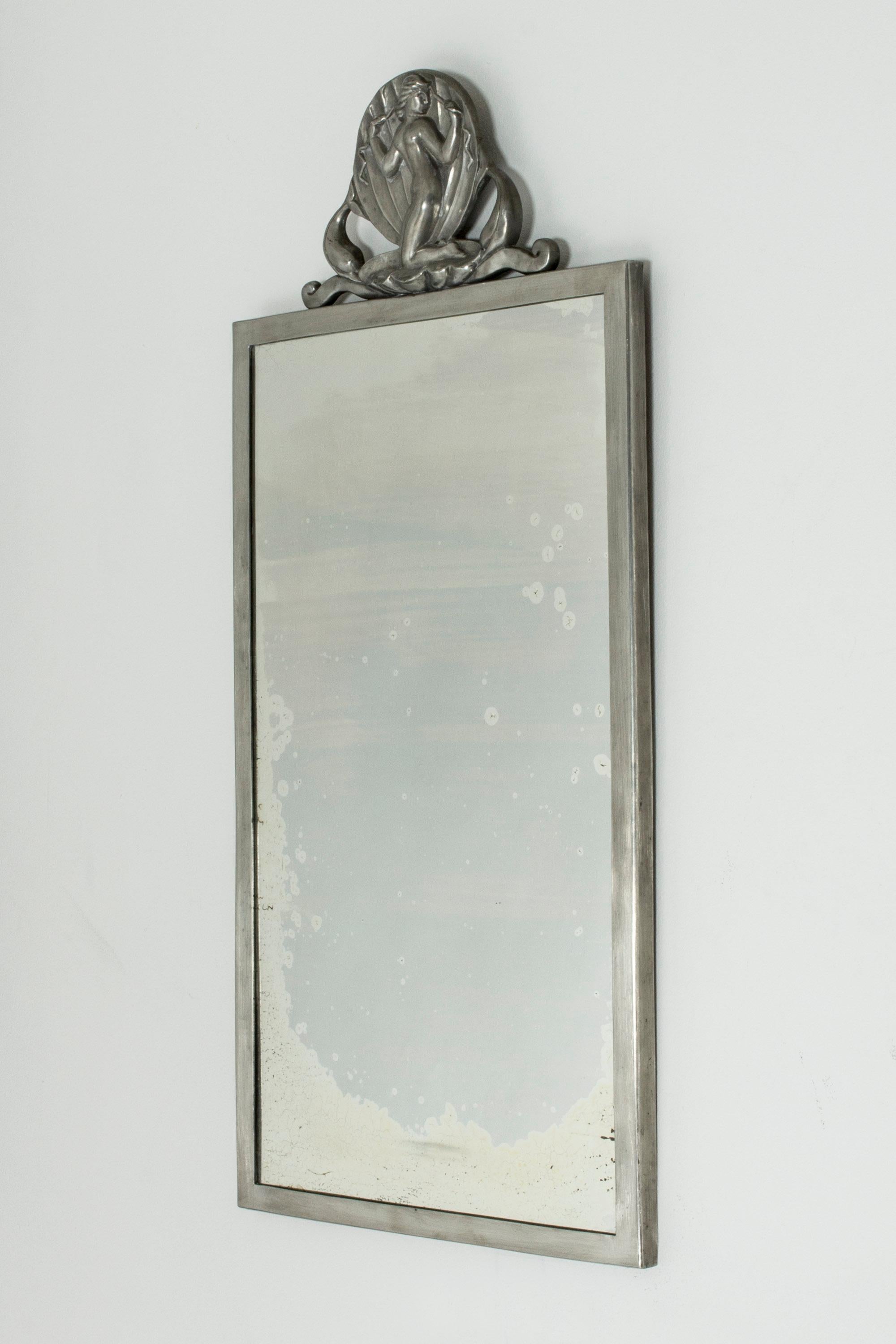 Pewter wall mirror from Ystad Metall, in a strict, simple shape. Contrasting, elaborate decoration on top, showing a beautiful Venus inside a shell, flanked by dolphins.

Literature: Eriksson, Jonas Barros. Ystad-Metall 1919-1969. Bokförlaget