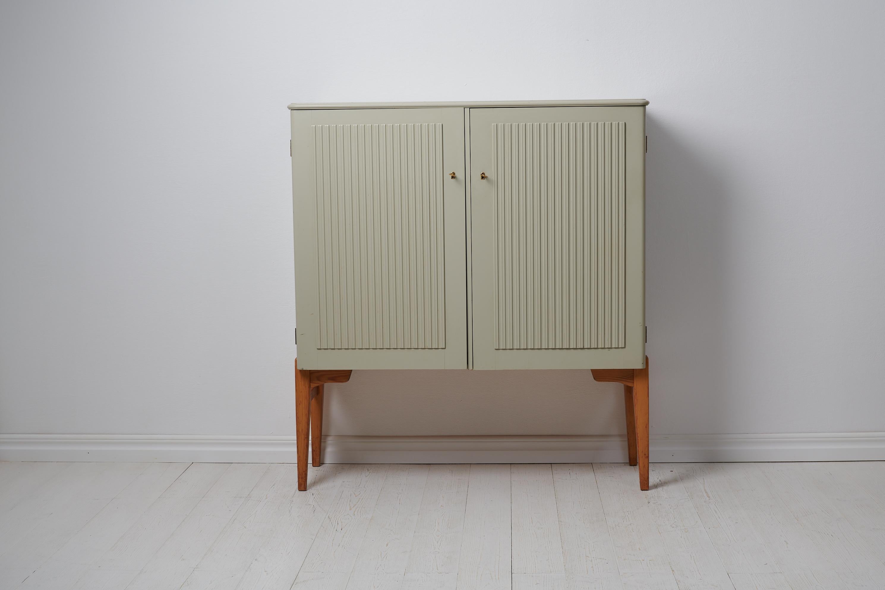 Swedish modern pine cabinet from the Mid-20th Century, around 1950 in painted Swedish pine. The legs of the cabinet are in bare wood which creates a contrast to the painted doors and frame. The doors have a fluted decor and open to an interior with
