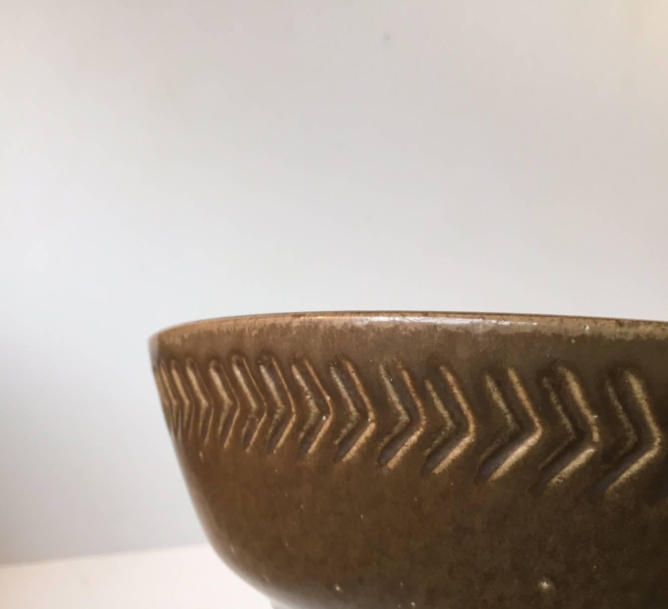 Stoneware bowl designed in 1954 by Swedish ceramist Yngve Blixt and manufactured by Höganäs. Decorated with incised geometric arrow motif around the perimeter on a caramel brown glaze that fades into a soft tone around the edge. This piece is signed