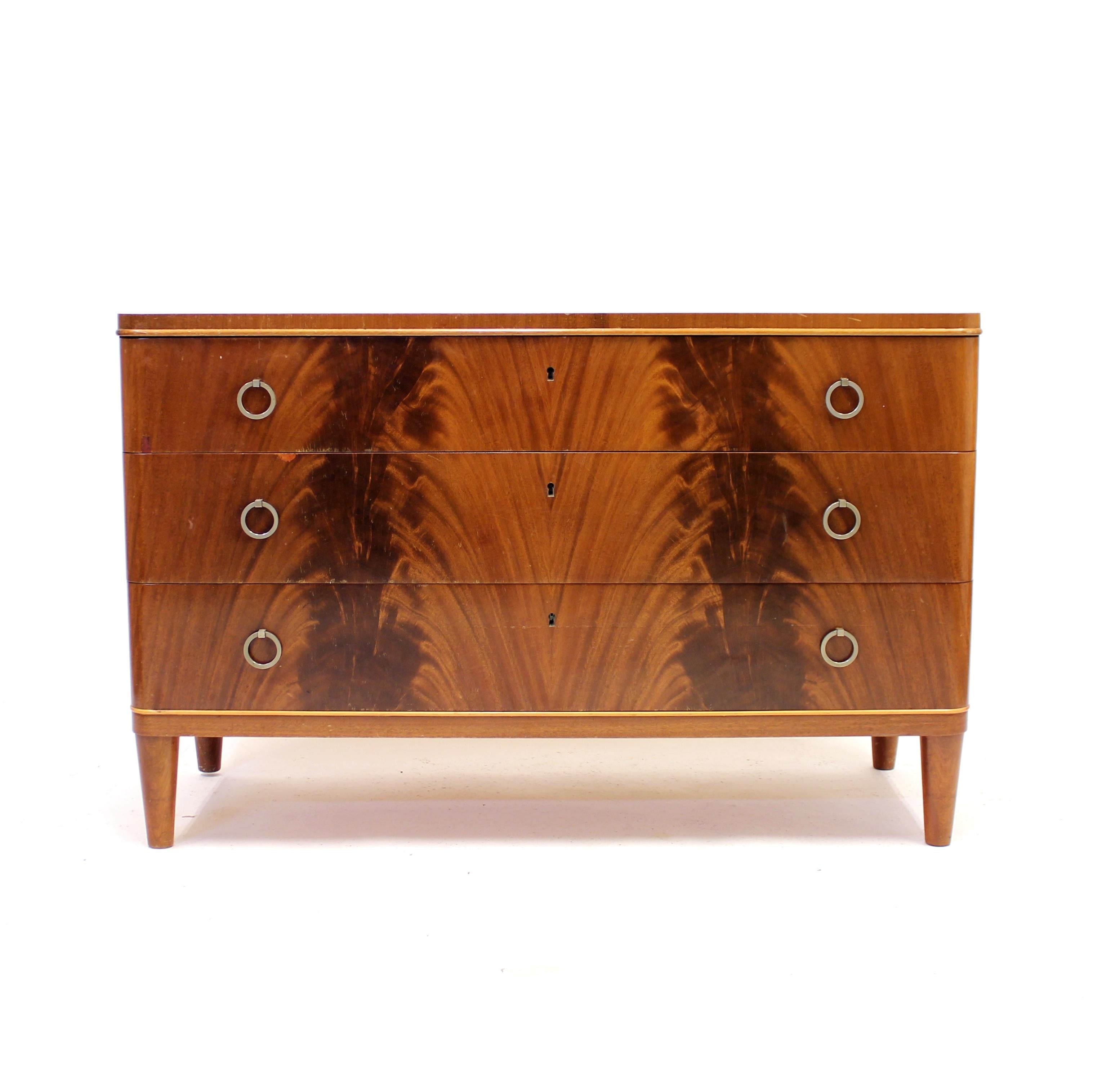 Swedish Modern chest of drawers in book matched Pyramid Mahogany from the 1940s. Very nice mahogany pattern on the frontside of the three equally sized drawers. Every drawer with two original round metal handles. Two strips of lighter wood, most