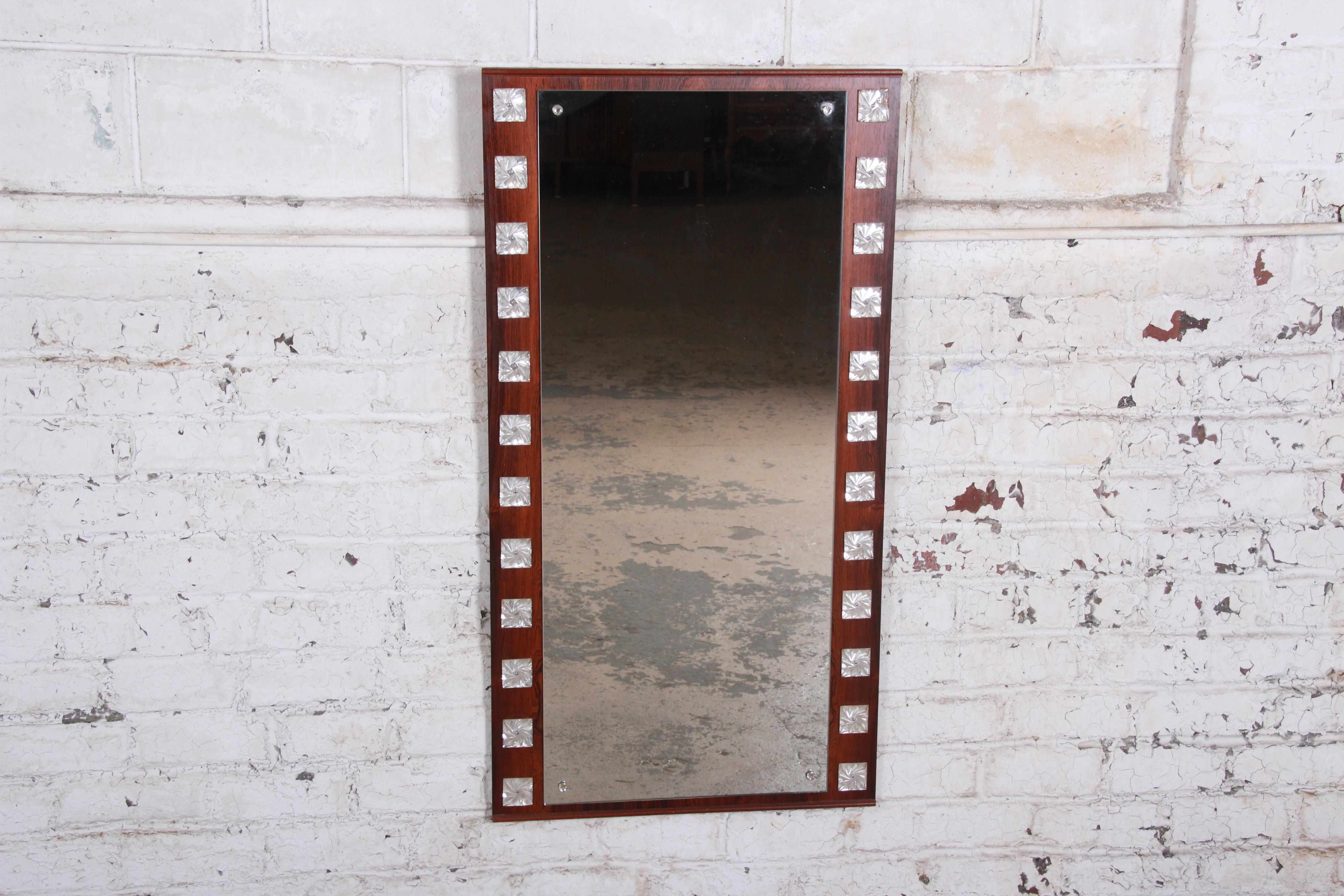 A gorgeous midcentury Swedish modern mirror designed by Erik Höglund for Eriksmålaglas of Sweden. The mirror features a stunning rosewood frame with decorative prisms on each side. The original label is present on the backside. The mirror is in very