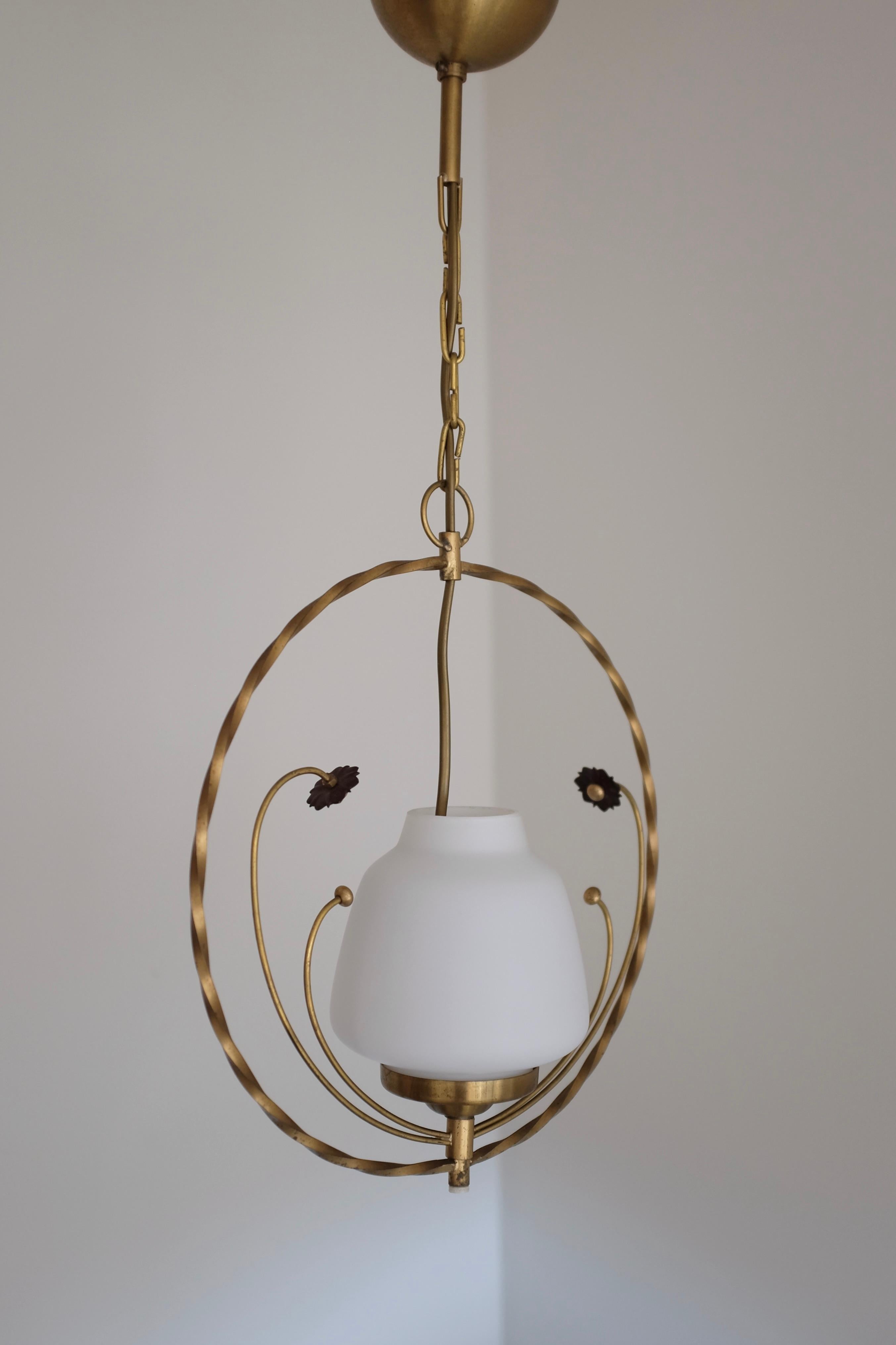 Affascinante ciondolo rotondo degli anni '50 in ottone e vetro con ornamento floreale organico. Con dettagli decorativi come l'ottone attorcigliato intorno alla lampada e le decorazioni floreali, si rifà molto allo stile del design moderno svedese