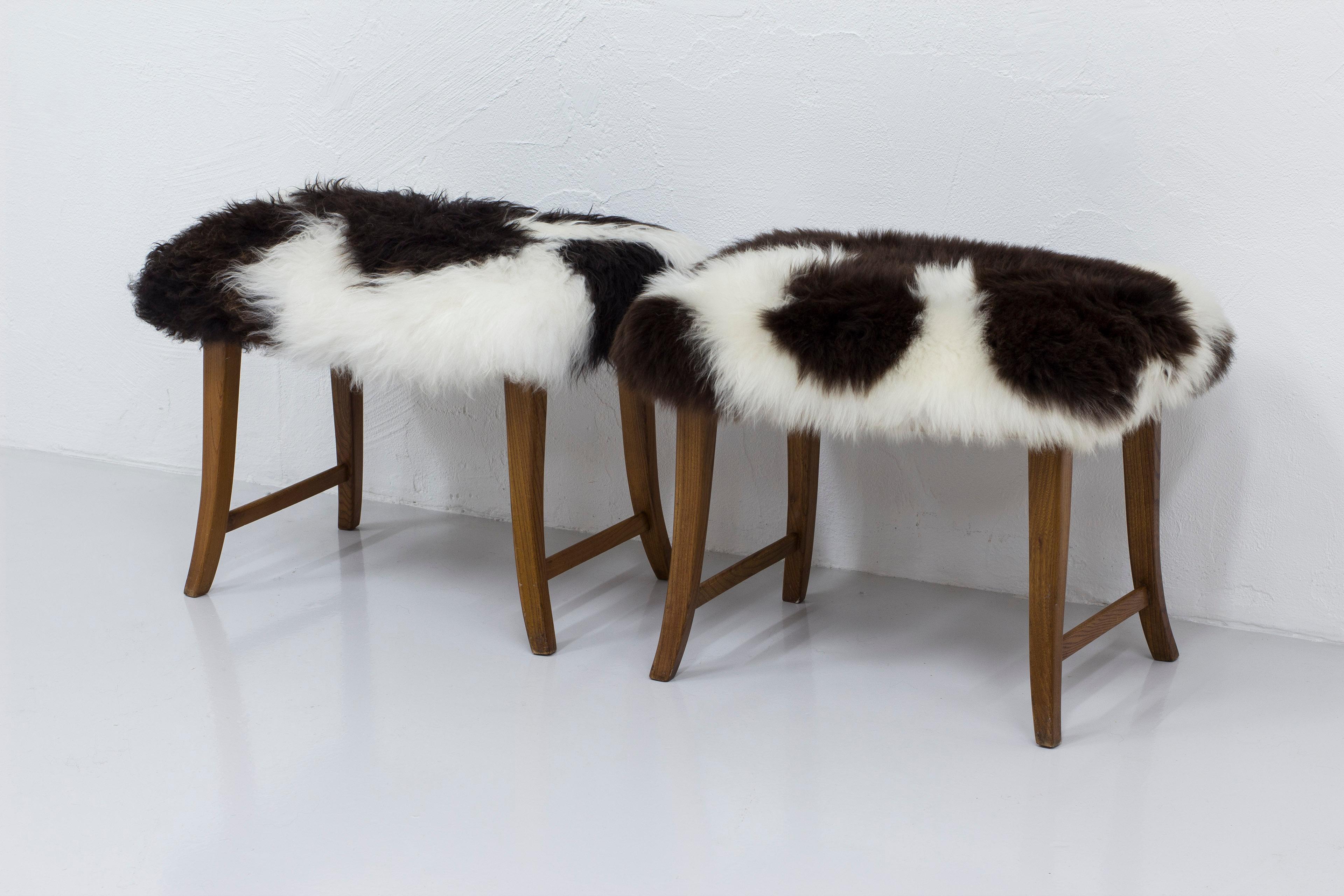 Pair of Swedish modern stools made ca 1940s. Curved and slightly tapered legs in solid elm. New upholstery in longhaired sheepskin with natural color. Works just as well as stools or footrests. Very good vintage condition with light age related wear