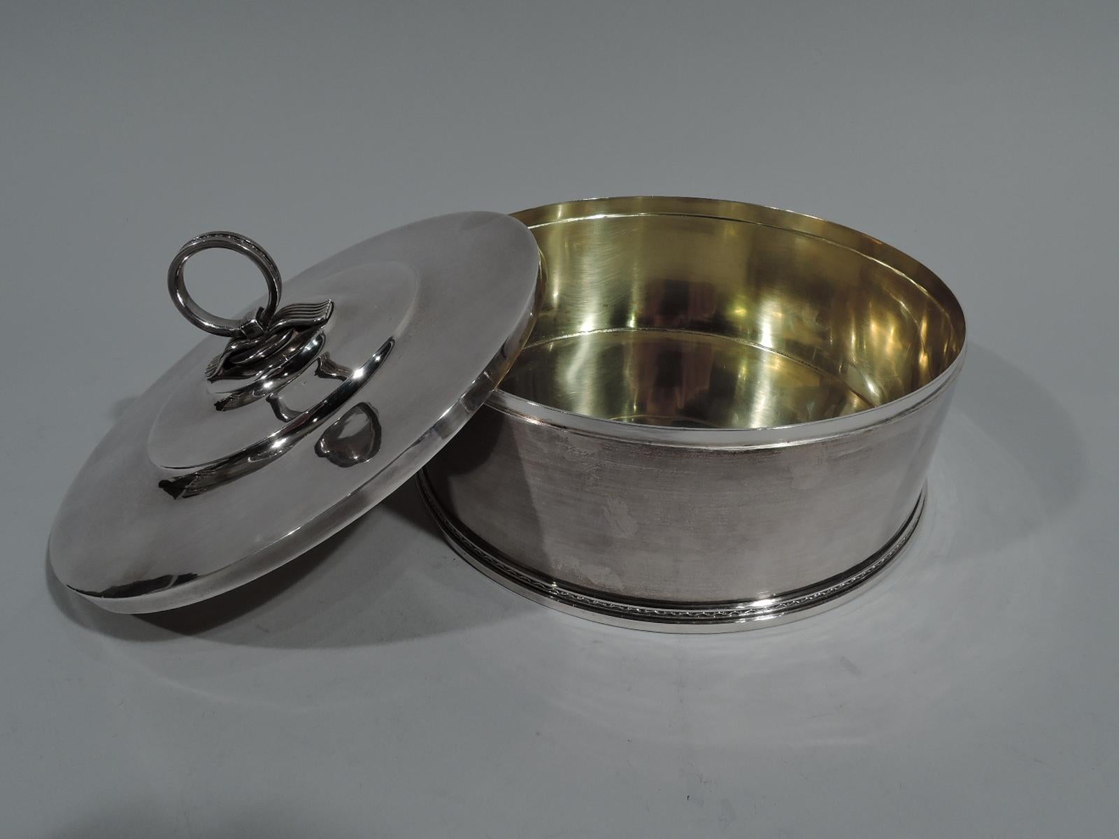 Modern sterling silver box. Made by Borgila in Sweden in 1936. Round with straight sides. Cover is flat and stepped with ring finial on reeded ribbon mount. Wire scalloping applied to finial and box base. Box and cover interior gilt washed.