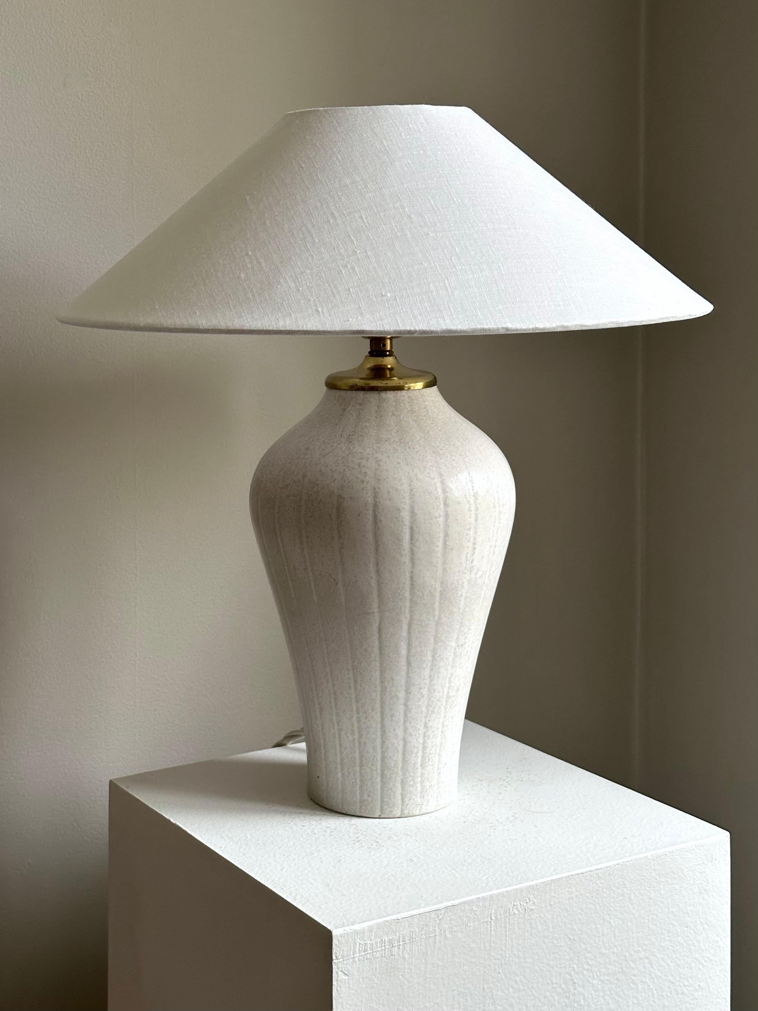 Elegant stoneware table lamp by Gunnar Nylund for Rörstrand, 1940s or 50s. Striped relief decor accenting the curved shape and a matte cream-white glaze with speckles. Marked 2nd factory sorting, likely due to a small defect in the glaze, see last