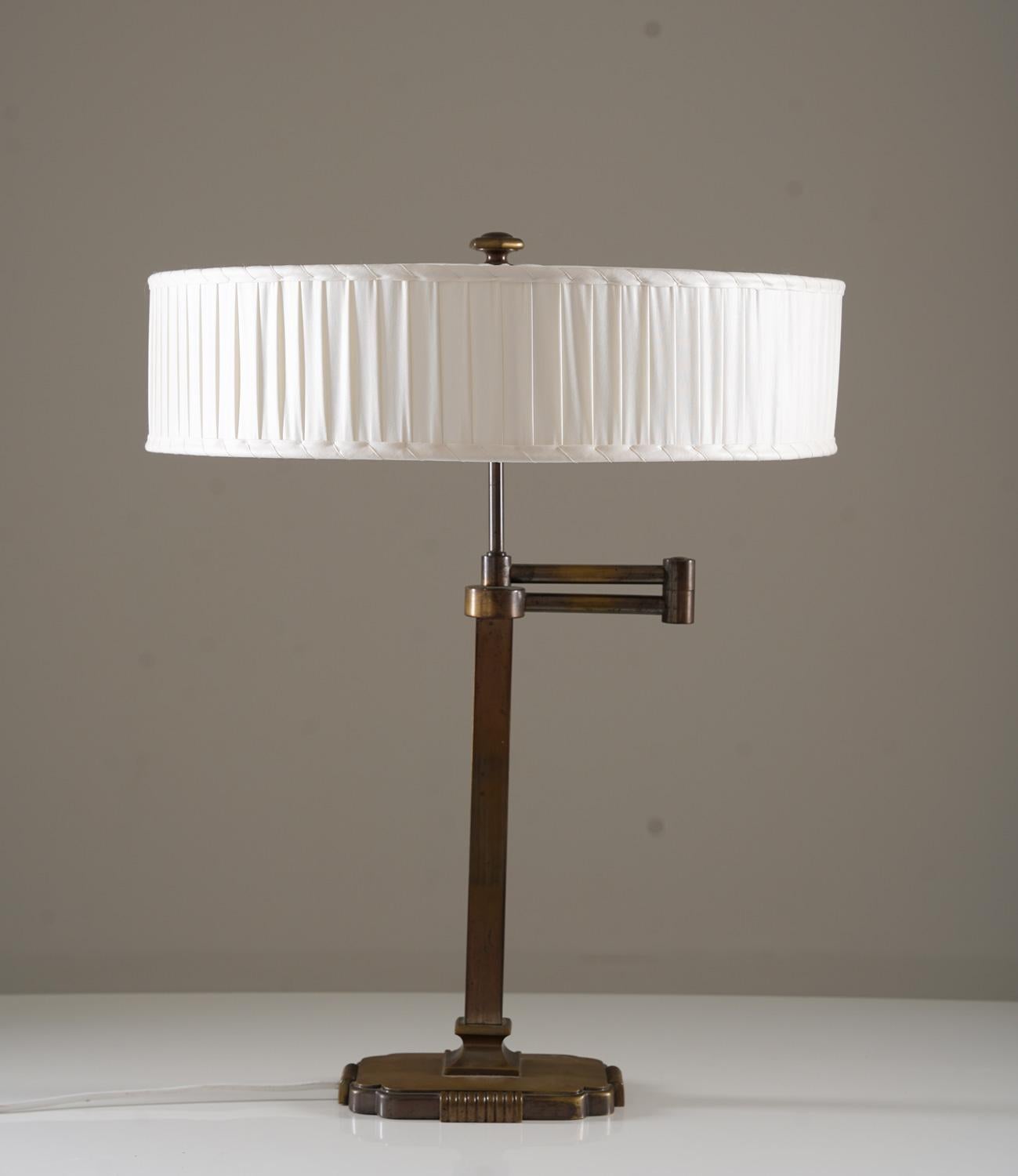 Swivel arm table lamp in brass manufactured in Sweden, 1940s. 
This elegant lamp was manufactured during the Swedish Modern era and is of very high quality. It is made of oxidized brass and has a large hand-pleated chintz shade.

Condition: Very