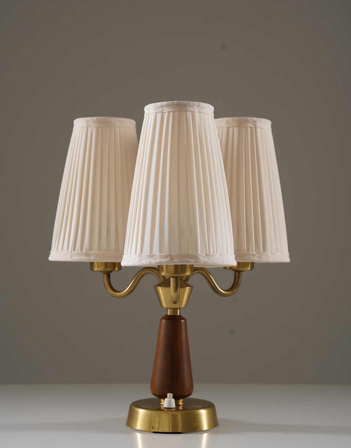 Swedish table lamp manufactured by ASEA in the 1940s. Made from brushed brass with a teak accent, it reflects the quality craftsmanship of the era. The lamp has three curved brass arms, each holding a newly pleated shade made from vintage chintz