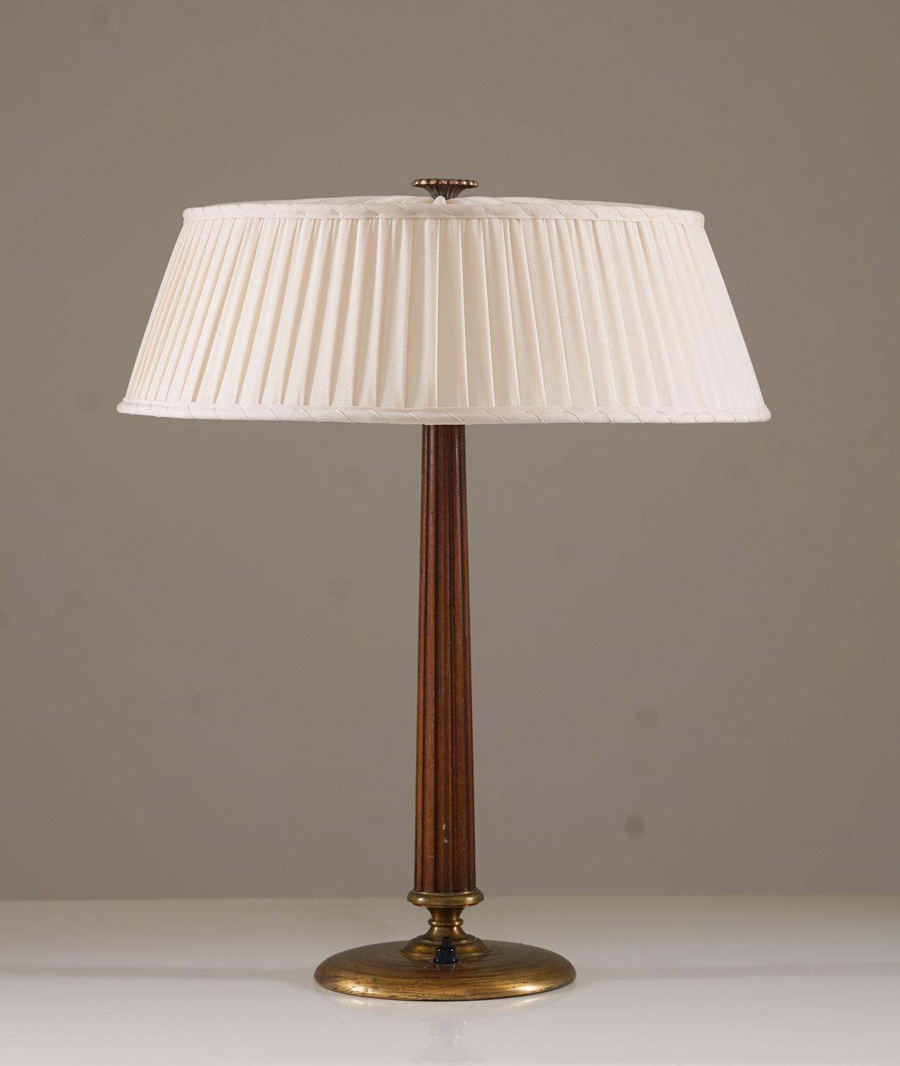 This elegant Swedish Modern table lamp, designed by Erik Tidstrand for Nordiska Kompaniet (NK) in the 1940s, exemplifies refined craftsmanship and timeless design. The lamp features a fluted walnut stem, gracefully complemented by a solid brass base