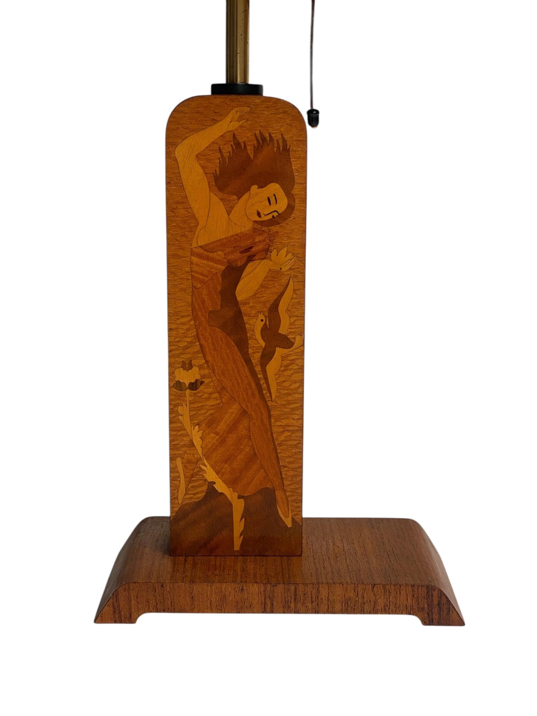 Cette lampe de table moderne suédoise de Mjölby Intarsia est un exemple frappant de l'artisanat des années 1930/40. Conçu avec une base en bois magnifiquement incrustée représentant un personnage expressif parmi des oiseaux et des fleurs, il met en