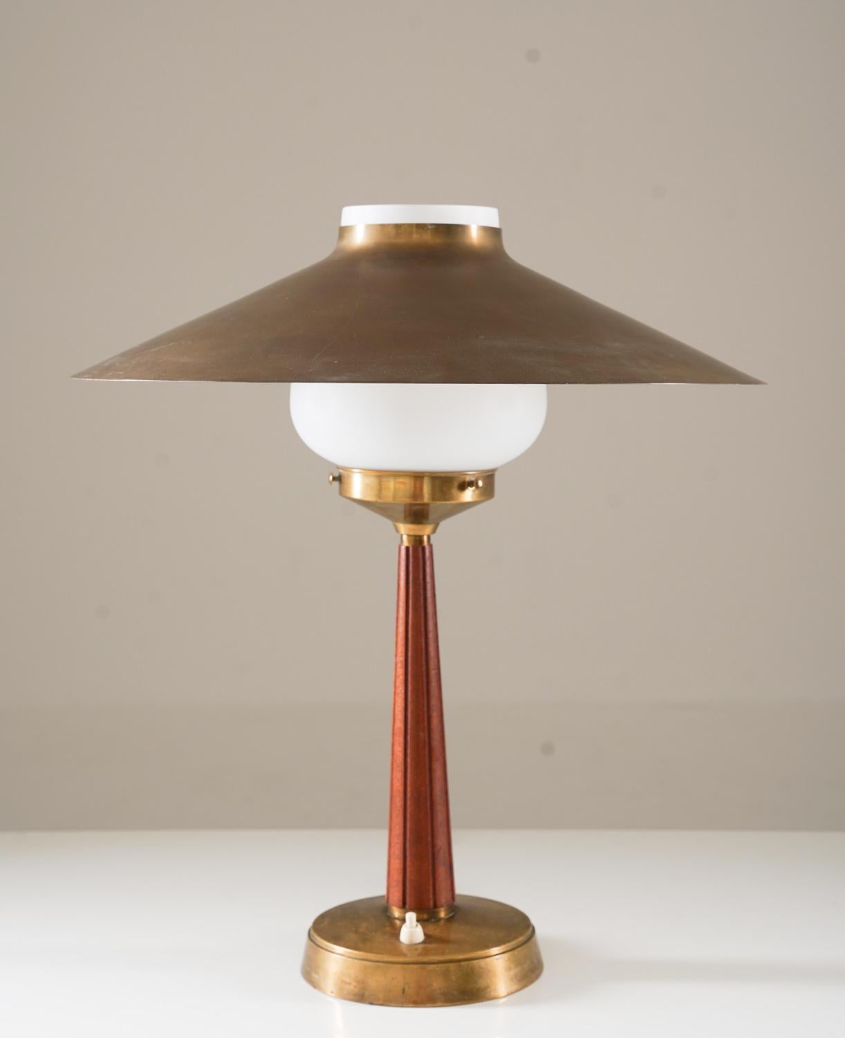 Élégante lampe de table scandinave par Elektro-Metall Malmö, Suède, années 1940.
Cette lampe est en laiton avec une tige en teck et un abat-jour en verre opalin. Le grand abat-jour en laiton repose sur l'abat-jour en verre, créant ainsi une belle