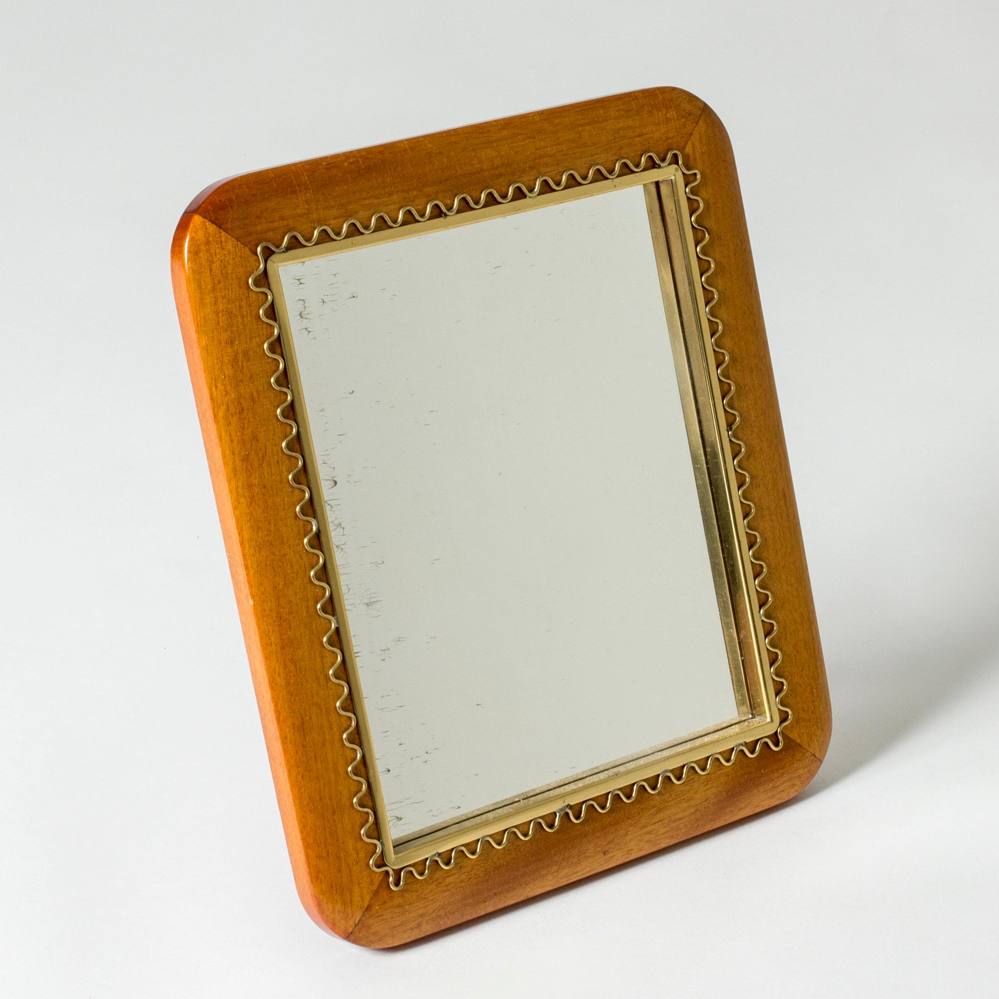 Lovely Swedish mid century table mirror. Made with a mahogany frame with rounded corners, decorated with a beautiful wave-shaped brass rim. Can also be hung on a wall.