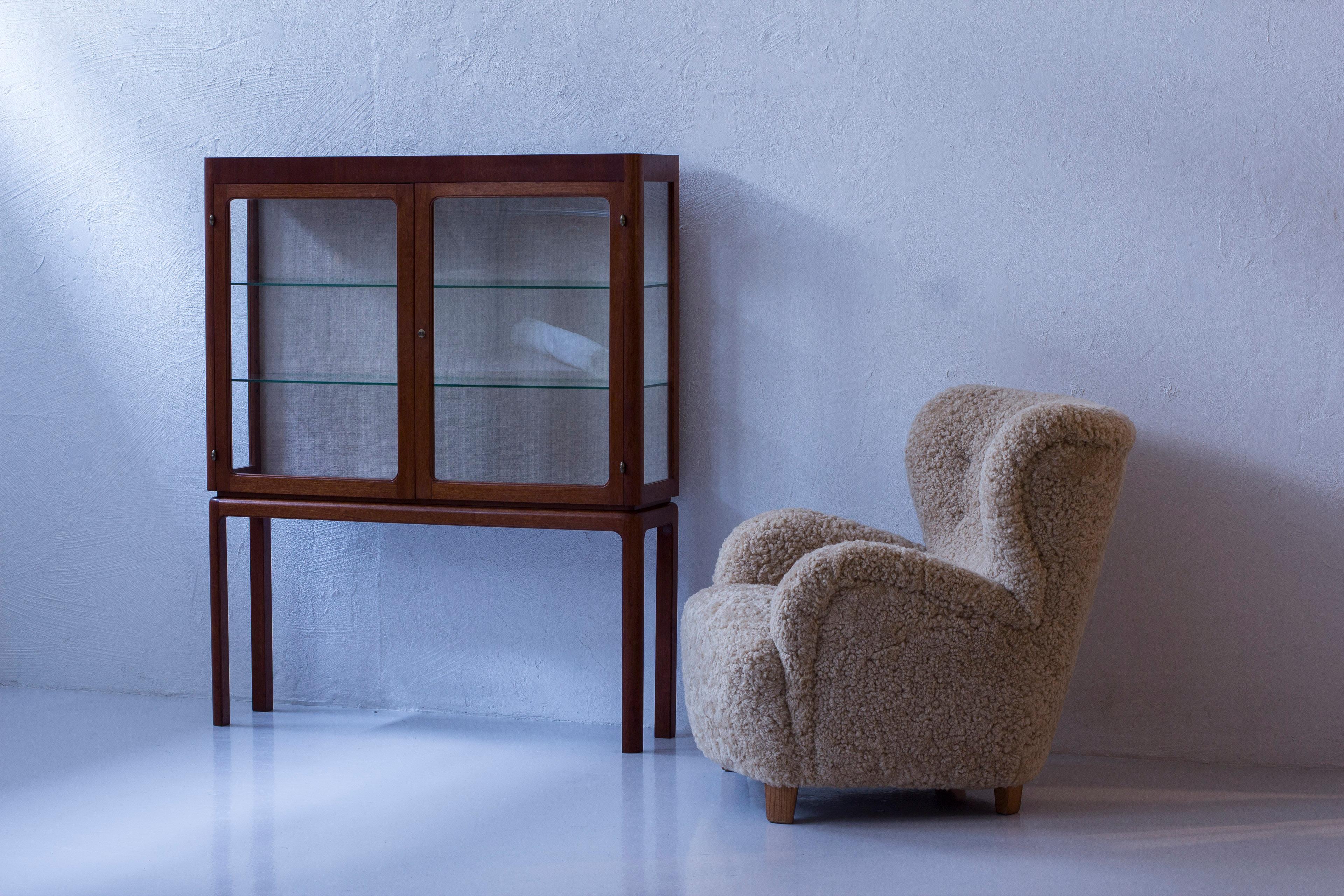 Schwedischer moderner Vitrinenschrank in der Art von Carl-Axel Acking. Produziert in Schweden in den 1940-50er Jahren. Hergestellt aus Mahagoni, Glas und Stoff. Messingbeschläge und -details im gesamten Schrank. Zwei verstellbare Glasböden. Der