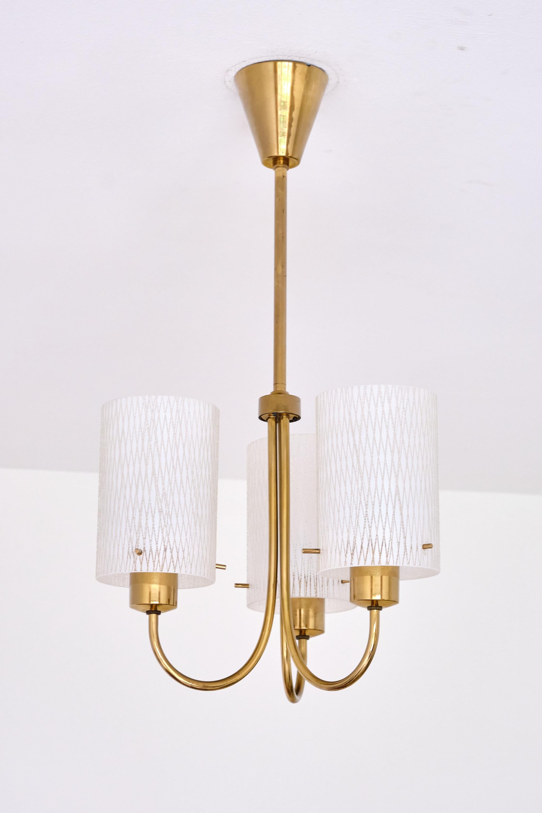 Questa elegante lampada a sospensione è stata progettata e realizzata in Svezia negli anni Cinquanta. 
Il design consiste in una sofisticata struttura curva a tre bracci realizzata in ottone di alta qualità, con i bracci che conducono a una