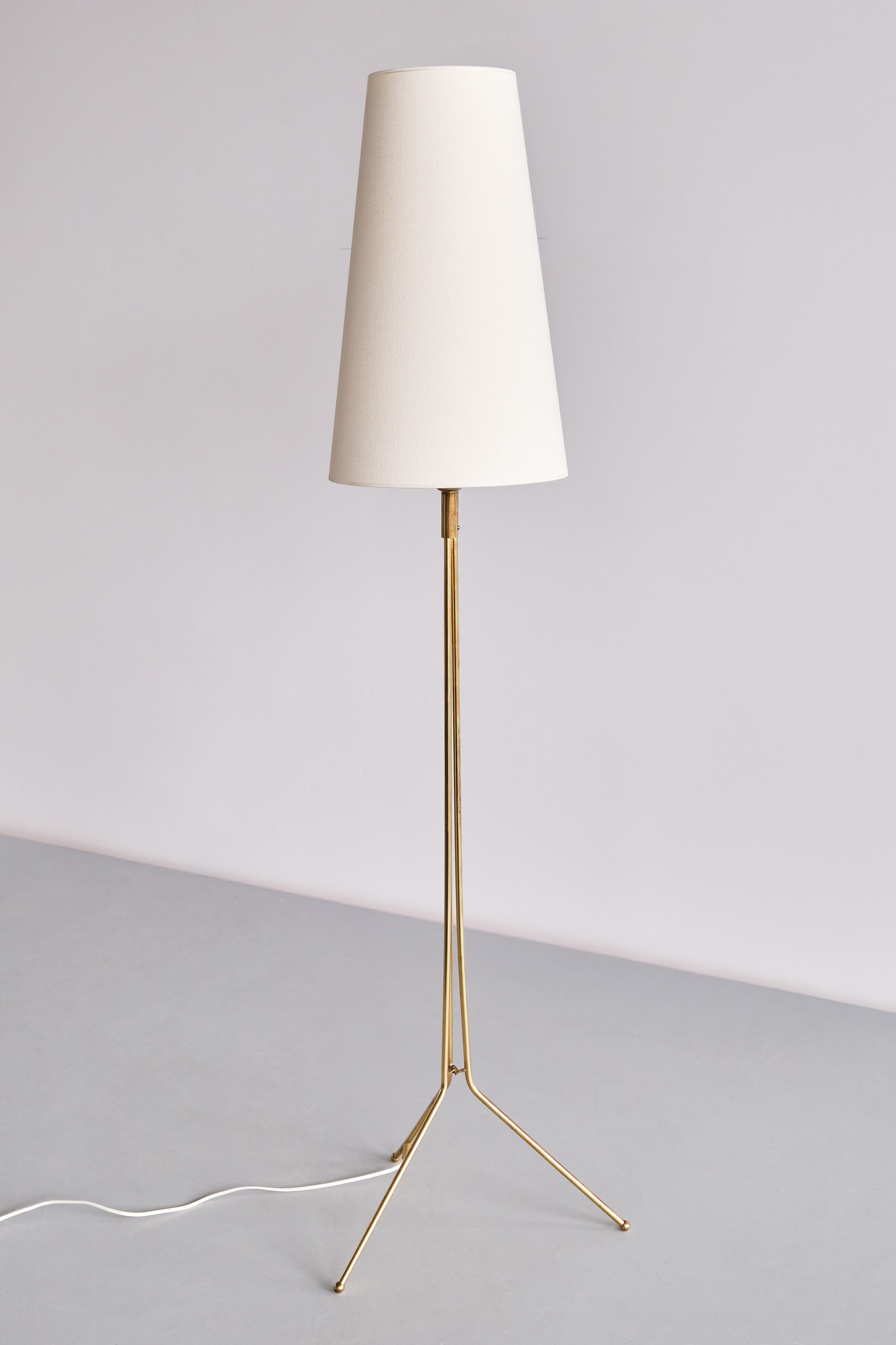 This elegant floor lamp was produced in Sweden in the 1950s. The design is marked by the tripod base, with the three brass legs continuing in three tubular stems which meet in the centre. The brass fitting with a button light switch. The cone shaped
