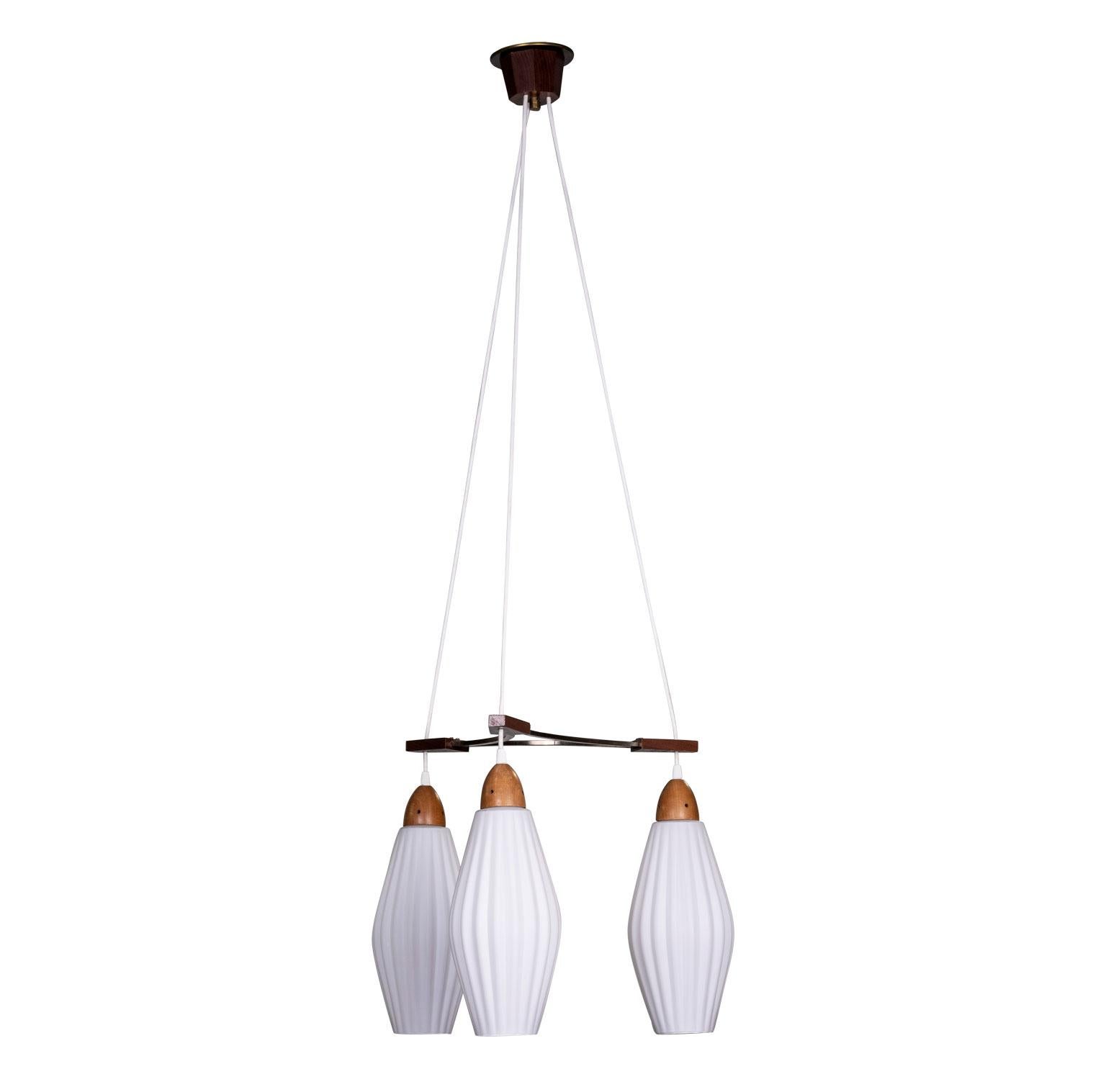 Swedish Mid-Century Modern triple pendant light by Luxus, circa 1960s. Teak and metal fixture with frosted glass shades. Newly wired for use within the USA using UL listed parts.