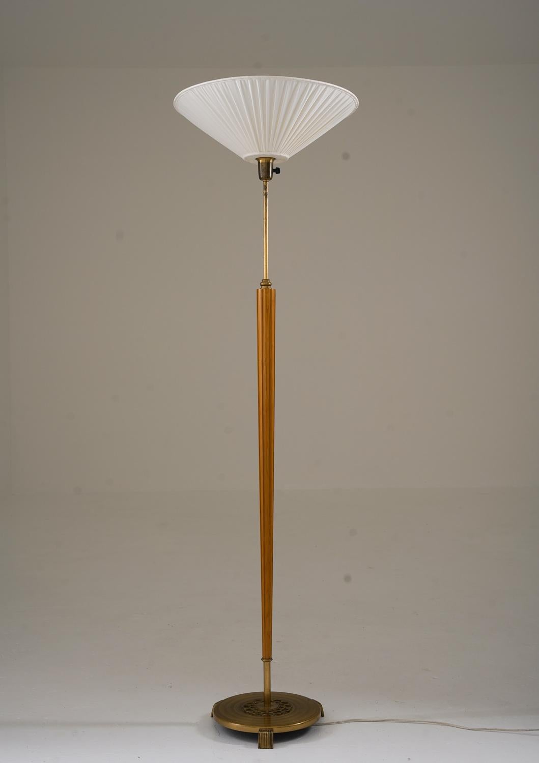 Swedish floor lamp from the 1940s with a combination of elm and brass. The slender, fluted rod in elm is complemented by brass details and a decorative, weighted base. The lamp is designed as an uplighter, providing a soft, ambient glow. The height