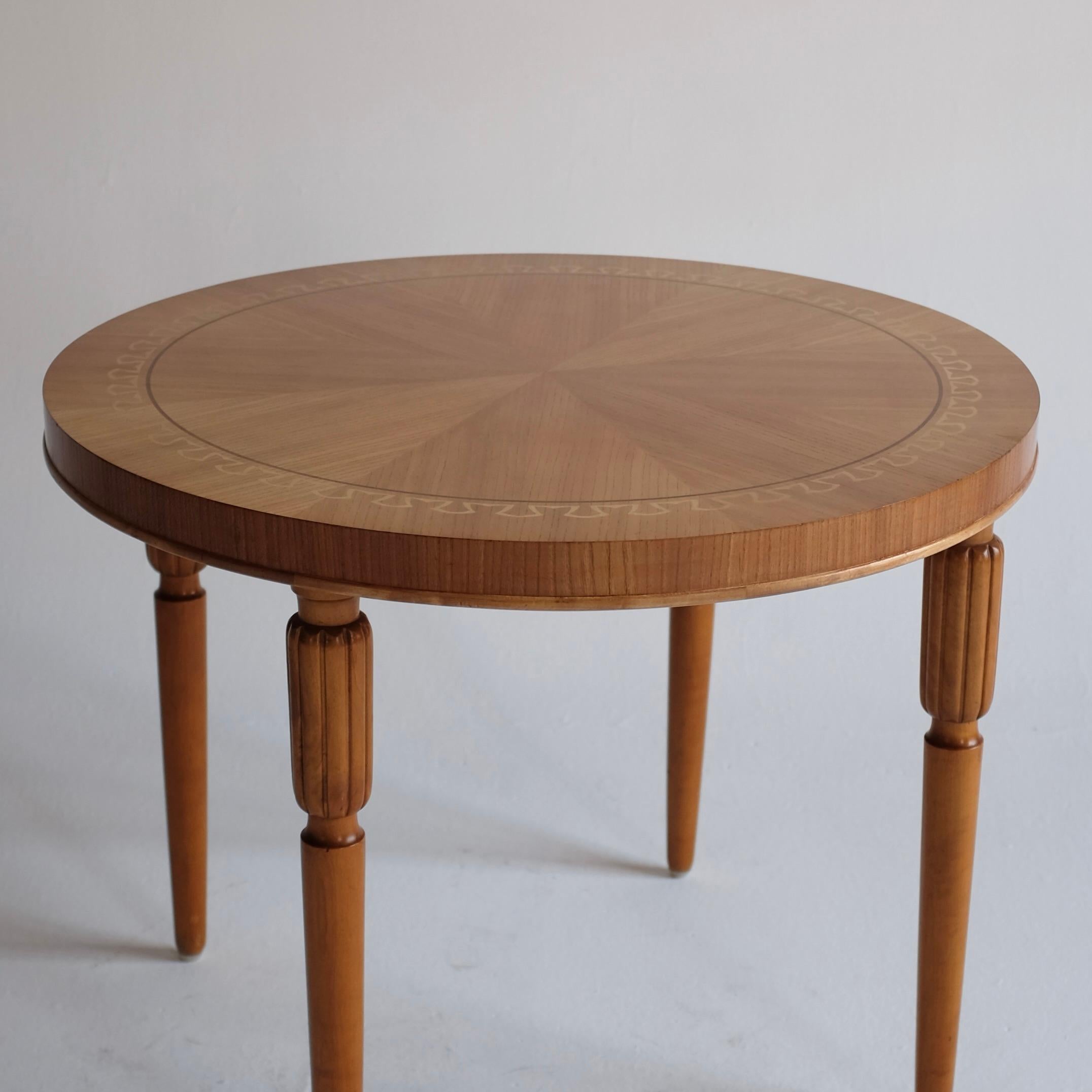 Swedish Modern Veneered Centre table from circa 1950s. Beautiful neo classic design around the edges in sycamore and cherry wood. Each leg with a carved top. The table has been re-finished and is in a very good condition with some small marks to the