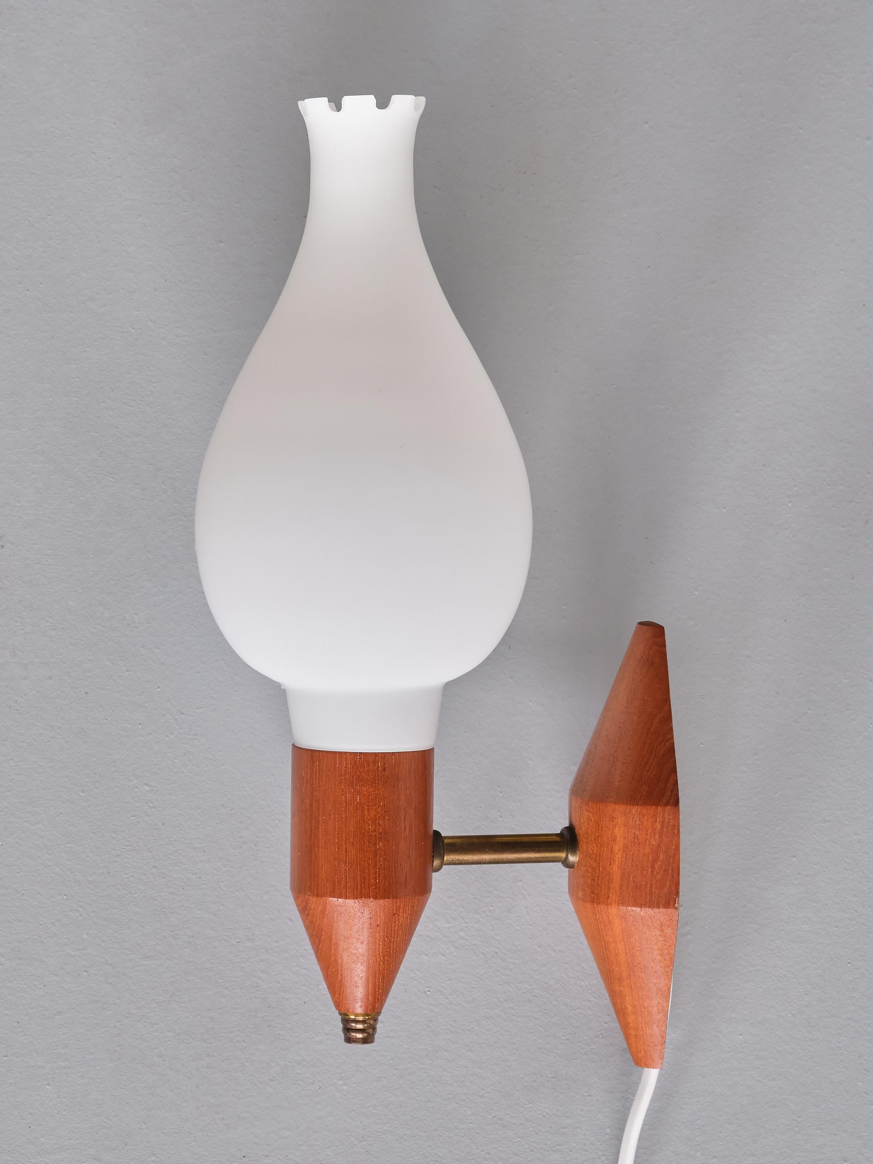 This elegant pair of wall lights was produced in Sweden in the 1950s. The design consists of a holder and back plate in solid teak wood, with a beautiful, warm grain. A nice detail is the arm and finial in brass. The matt white shades are tear