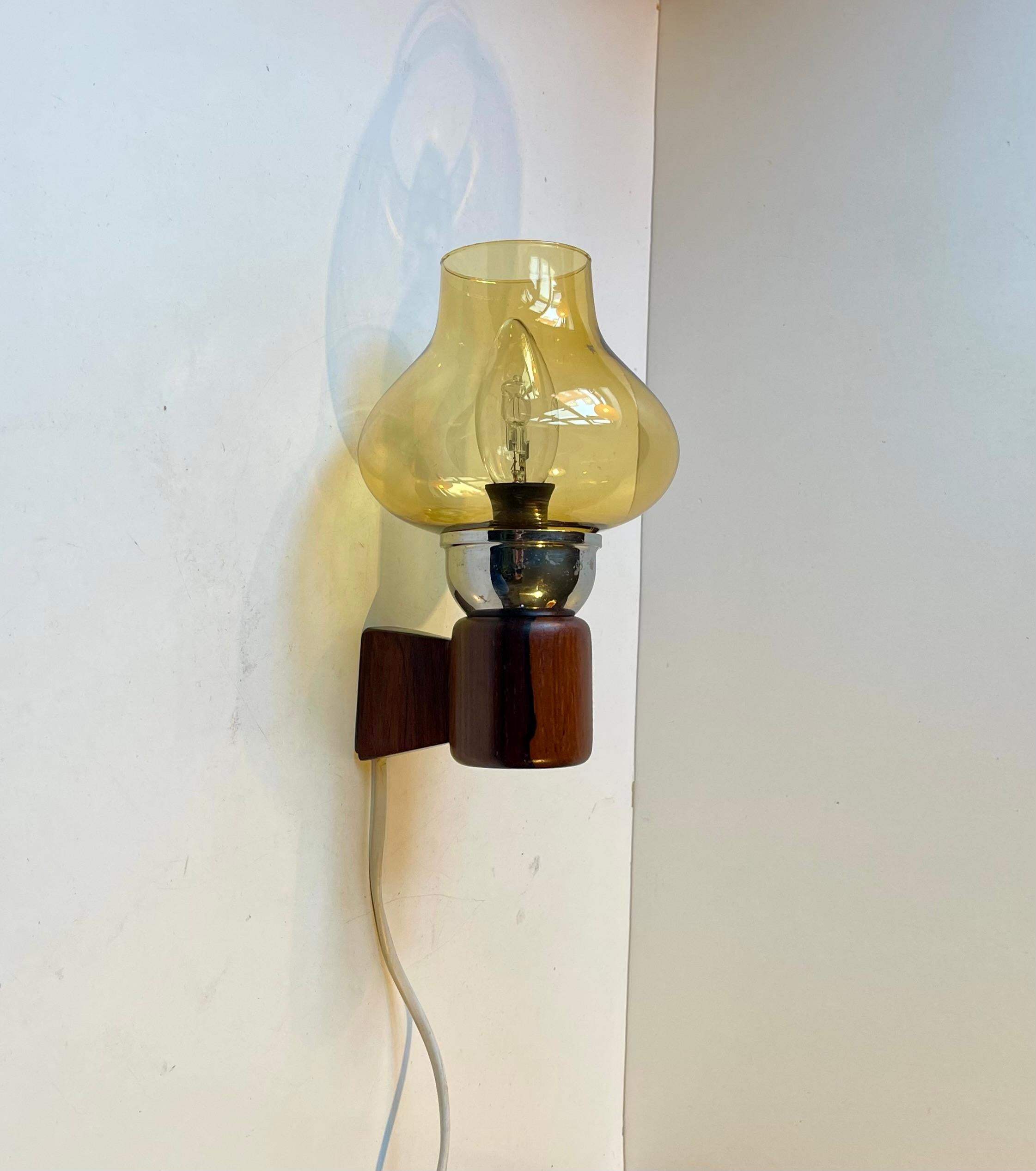 In the style of Uno & Osten Kristiansson comes this stylish wall light executed in engine-turned hard wood and featuring a yellow smoke glass shade. It was made in Sweden during the 1950s or 60s. 

Measurements: 19x13x10 cm (H/D/diameter).
